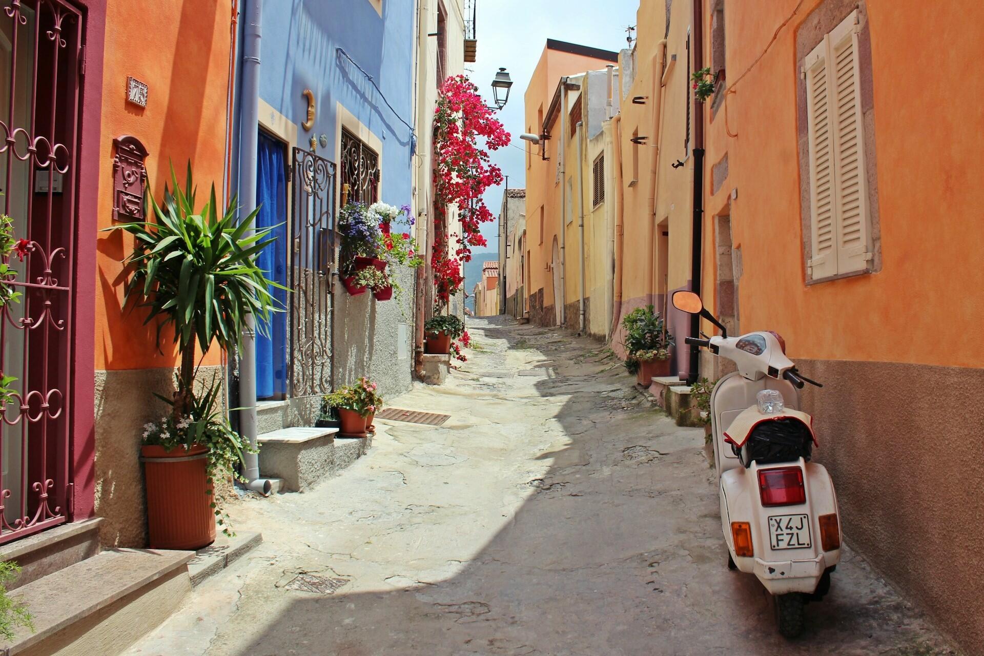 Colourful street in an Italian town with potted flowers and a parked scooter