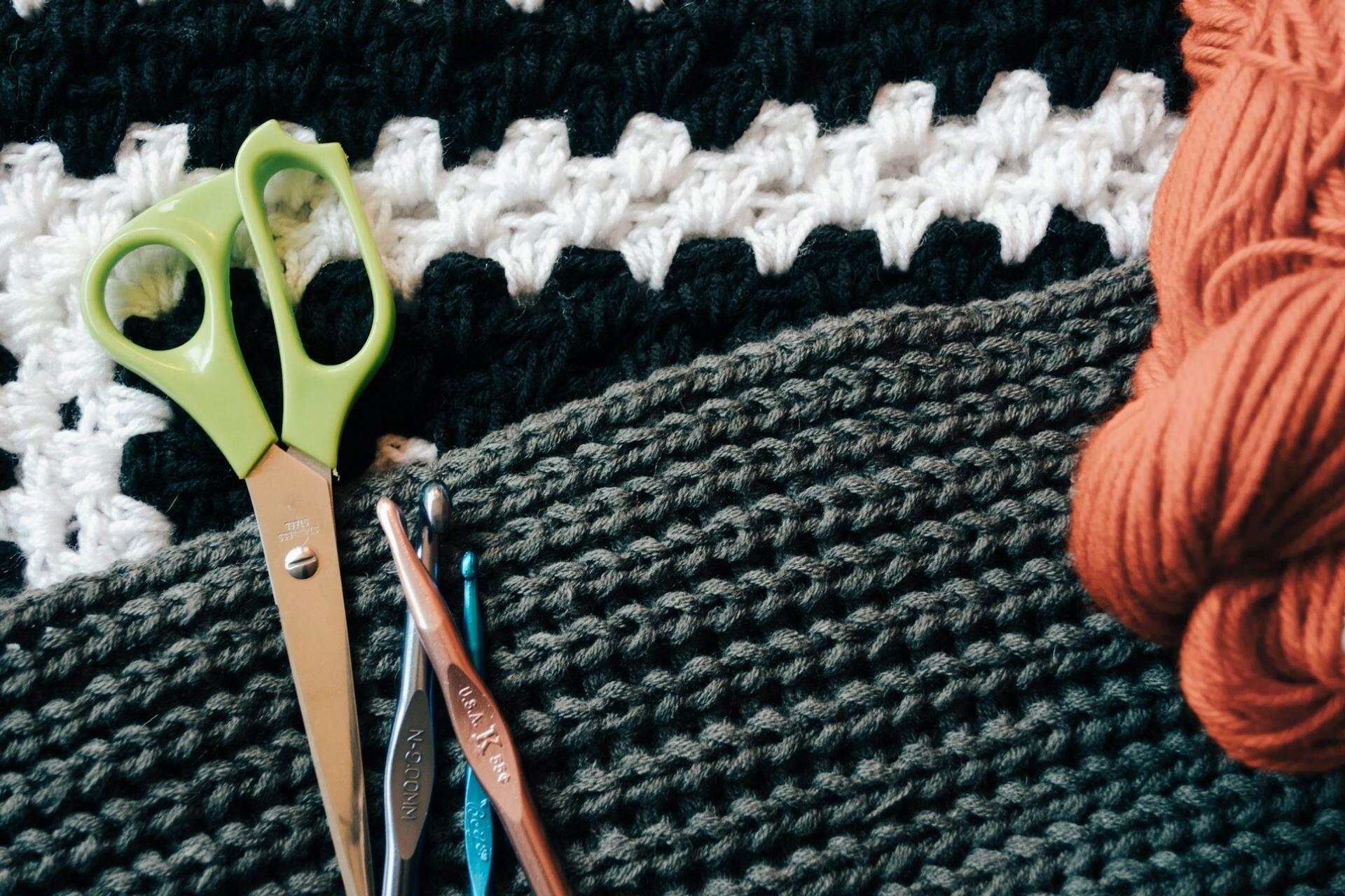 Green scissors, crochet hooks, orange yarn and crocheted fabric
