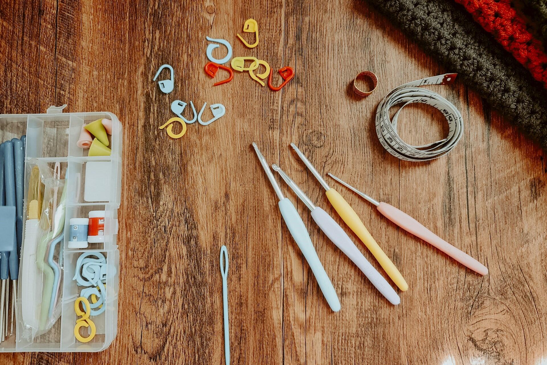 Crochet hooks, stitch markers, tape measure and craft tools on a wooden table