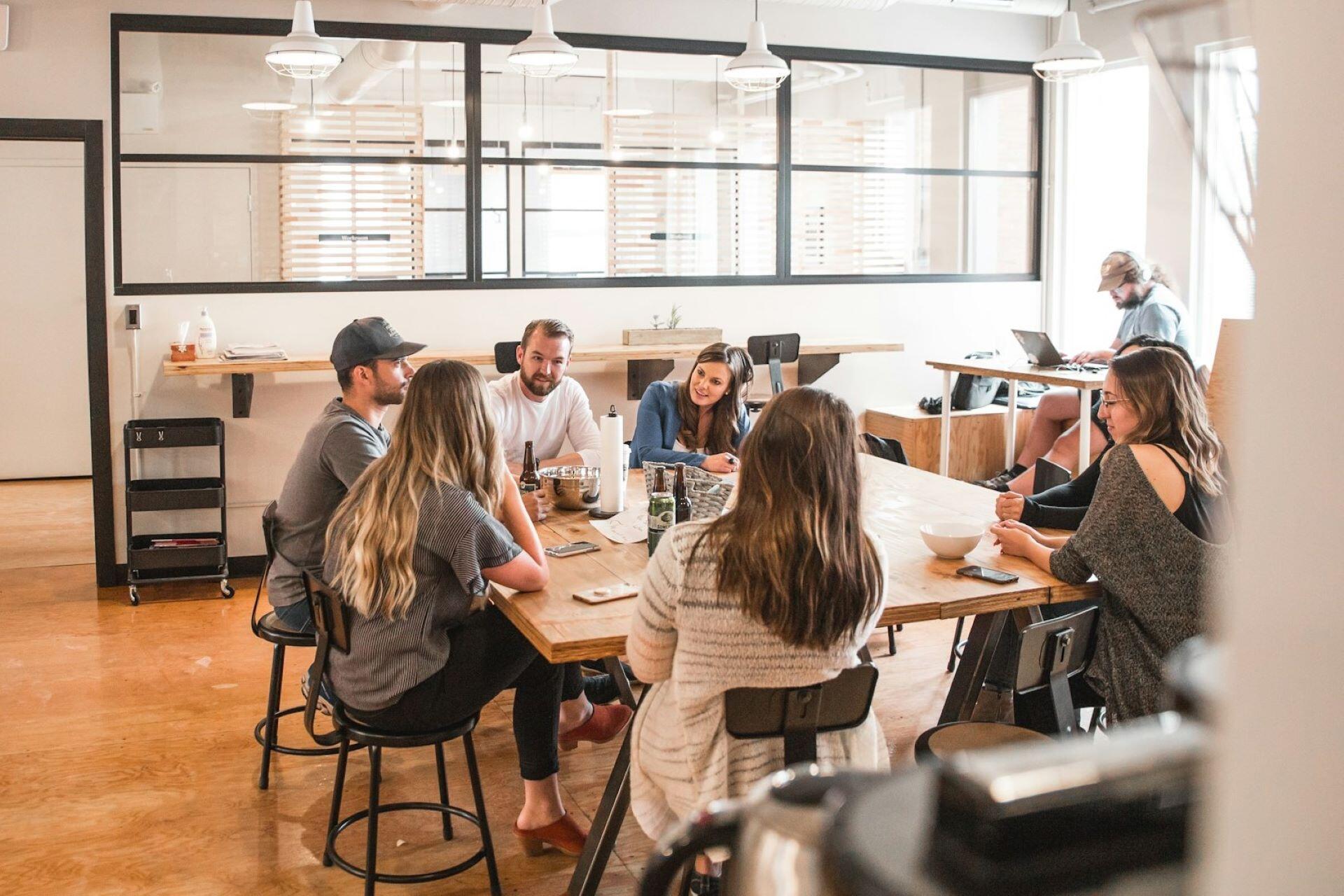 A group of people sitting around a wooden table in a bright office