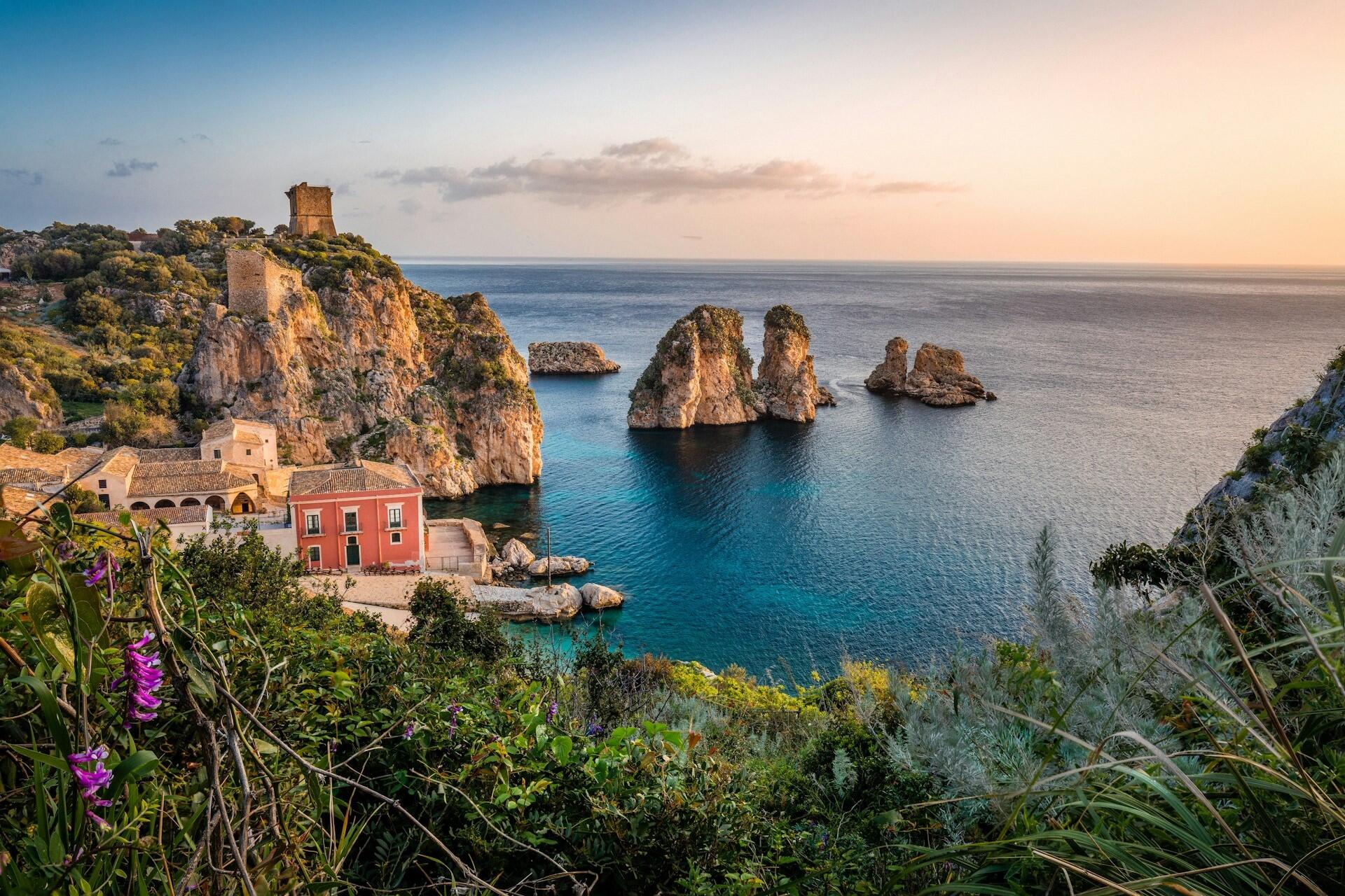 Rocky coastline with clear blue water and small buildings on a cliff in Italy