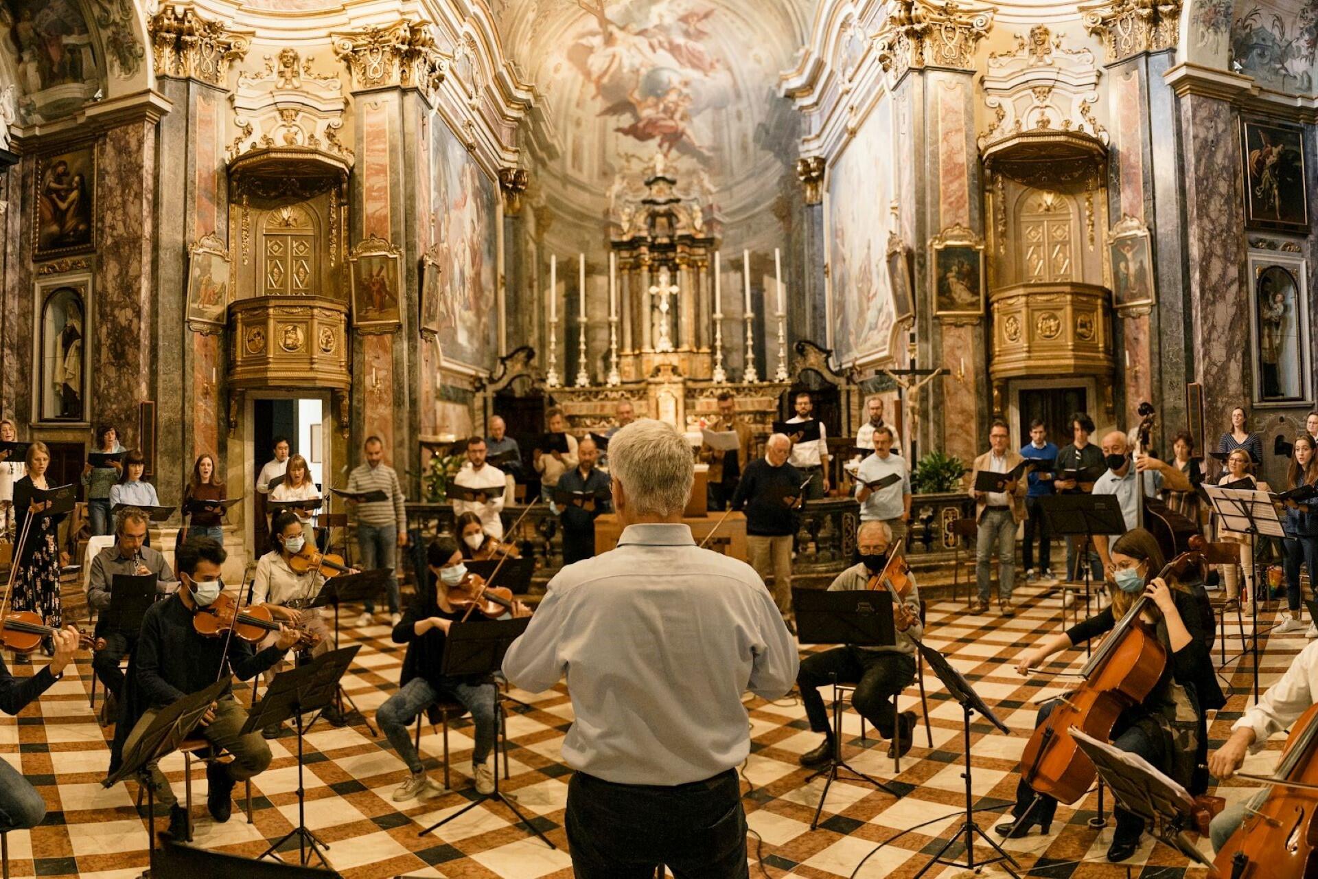 Orchestra and choir performing inside a decorated church with a conductor facing them