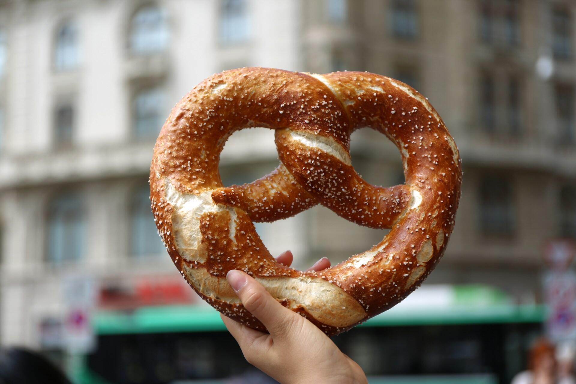 Hand holding a traditional German pretzel with blurred city background