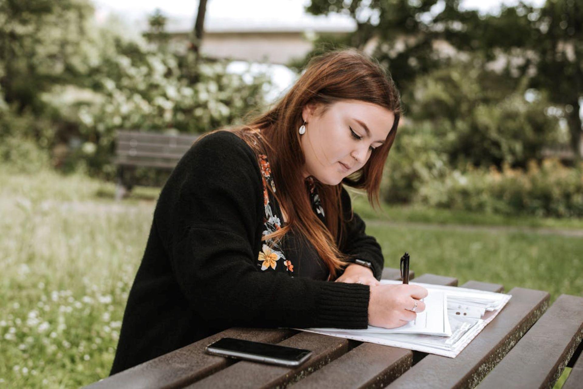 Woman writing in a notebook at a park table