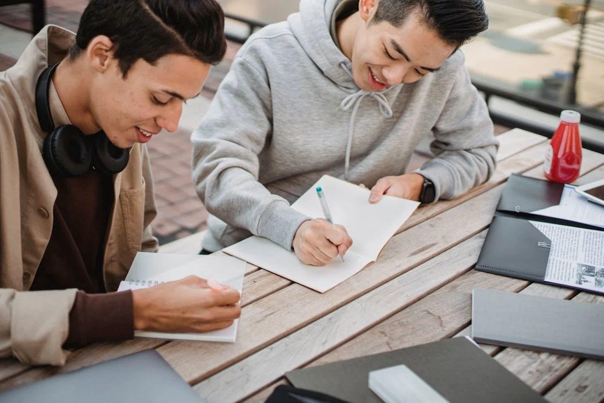Two students studying English together outdoors with notebooks