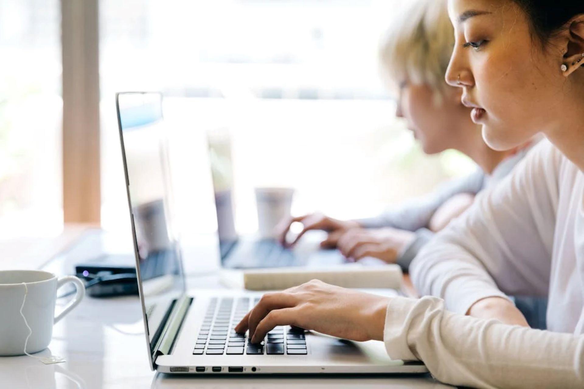 Two students using laptops in a bright workspace