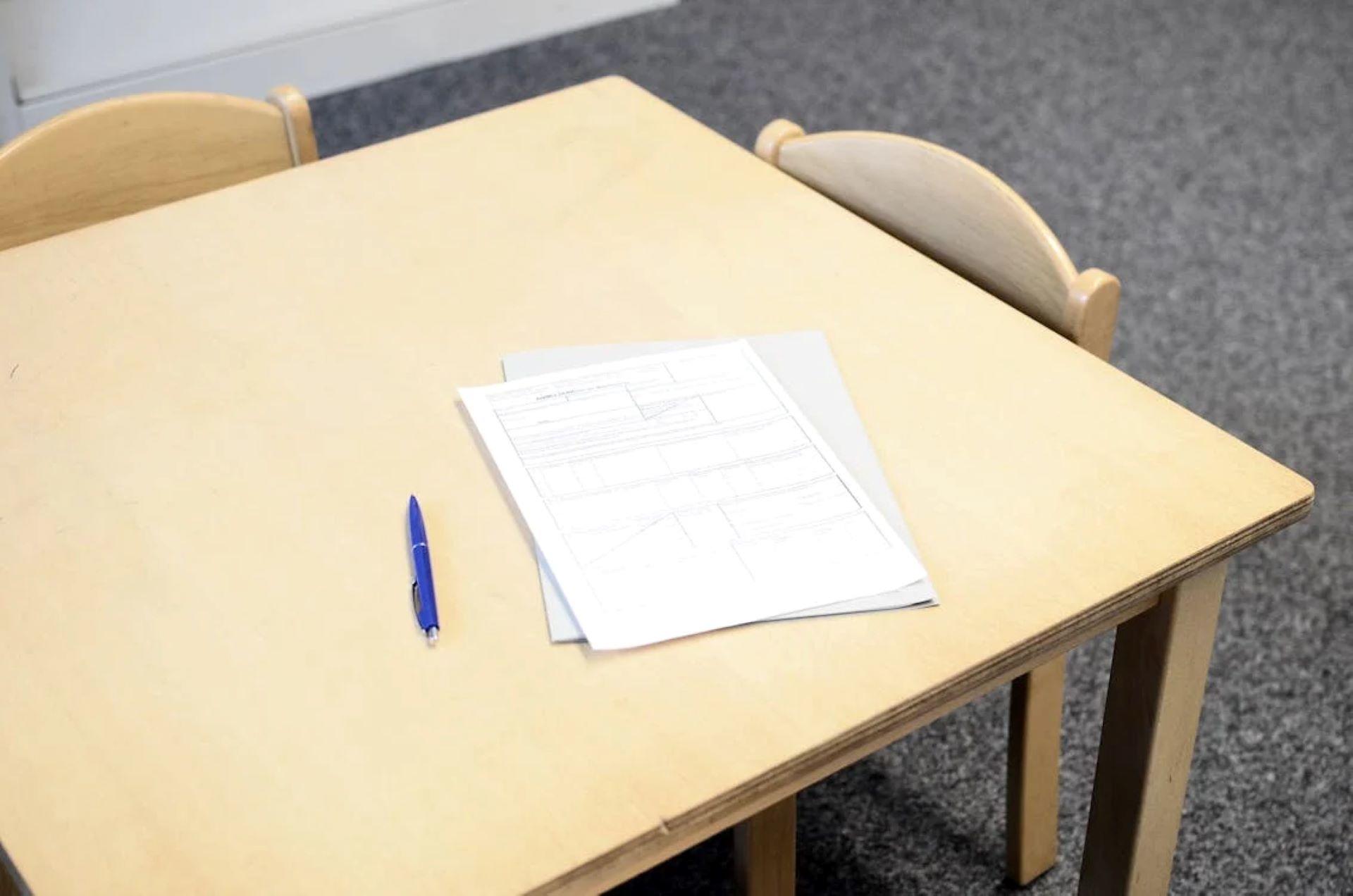 Classroom desk with papers, pen, and chairs