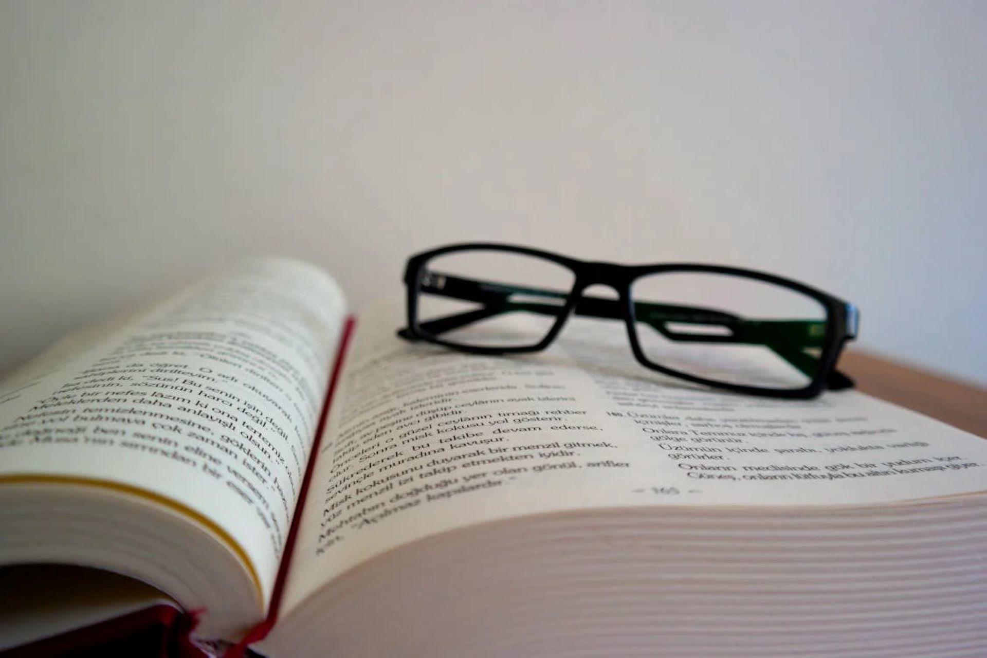 A book lying open on a desk with eyeglasses.