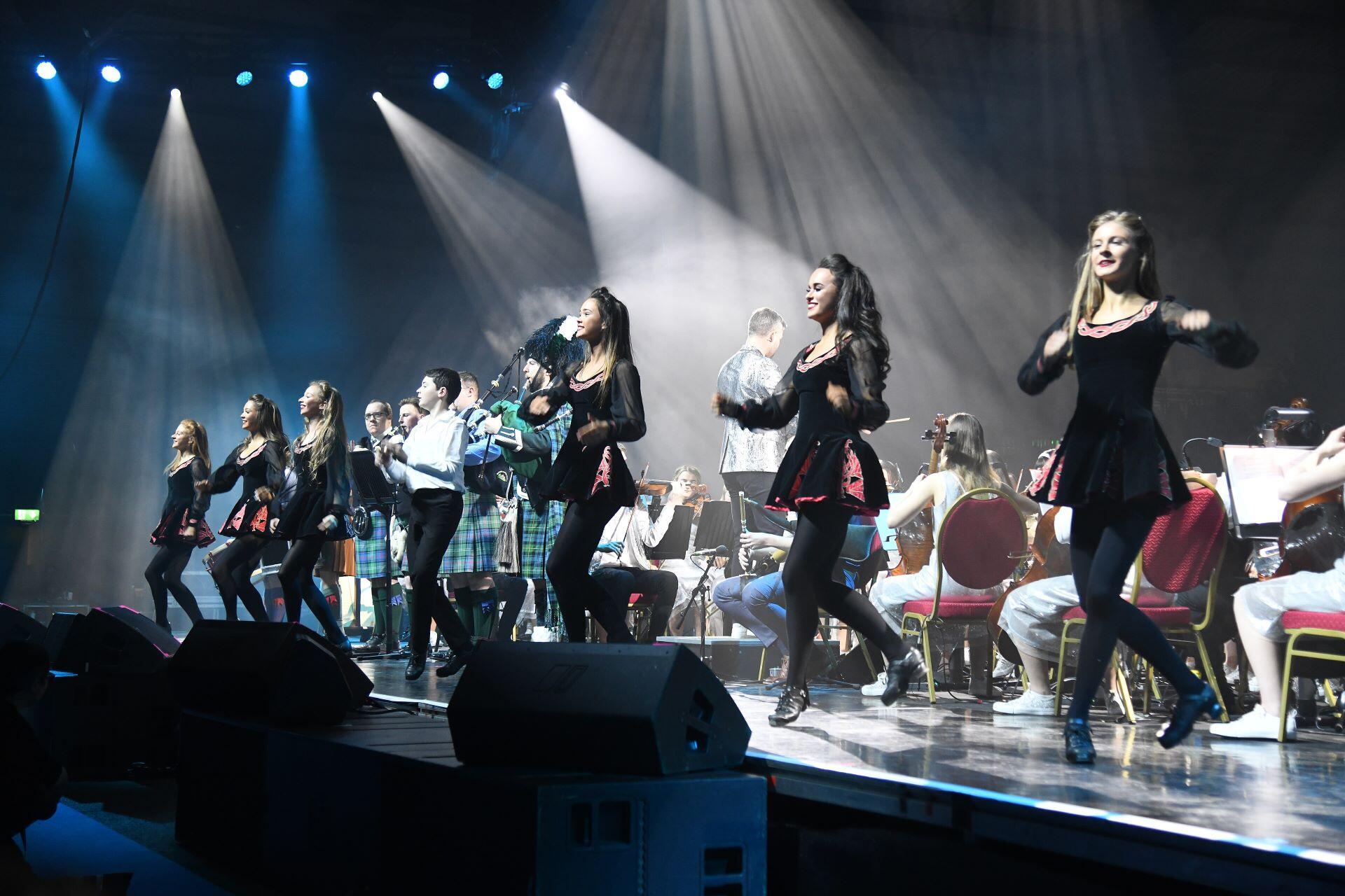 Irish dancers performing on a brightly lit stage with musicians behind them