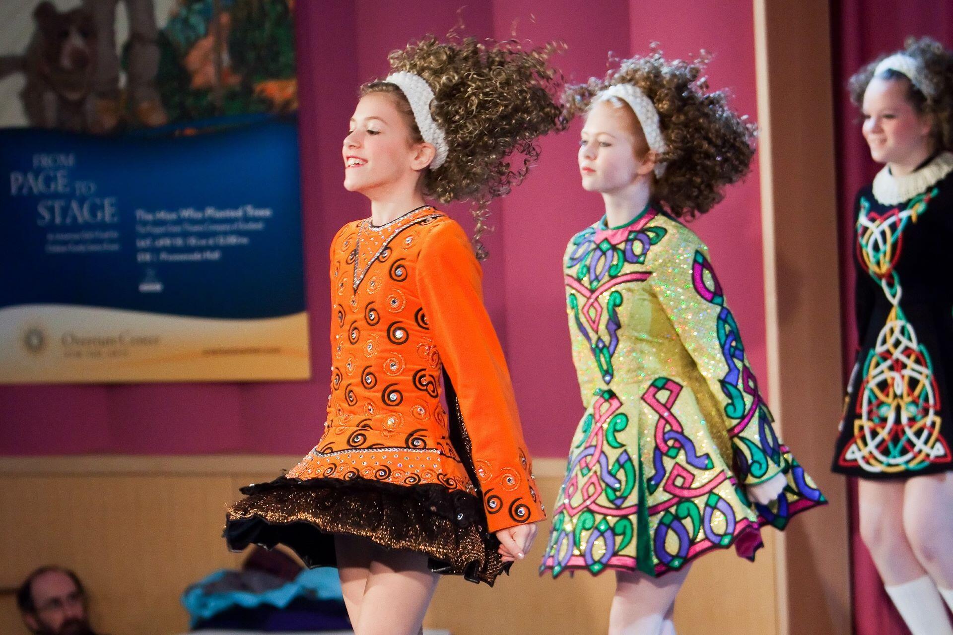 Three young Irish dancers performing on stage in colourful embroidered dresses