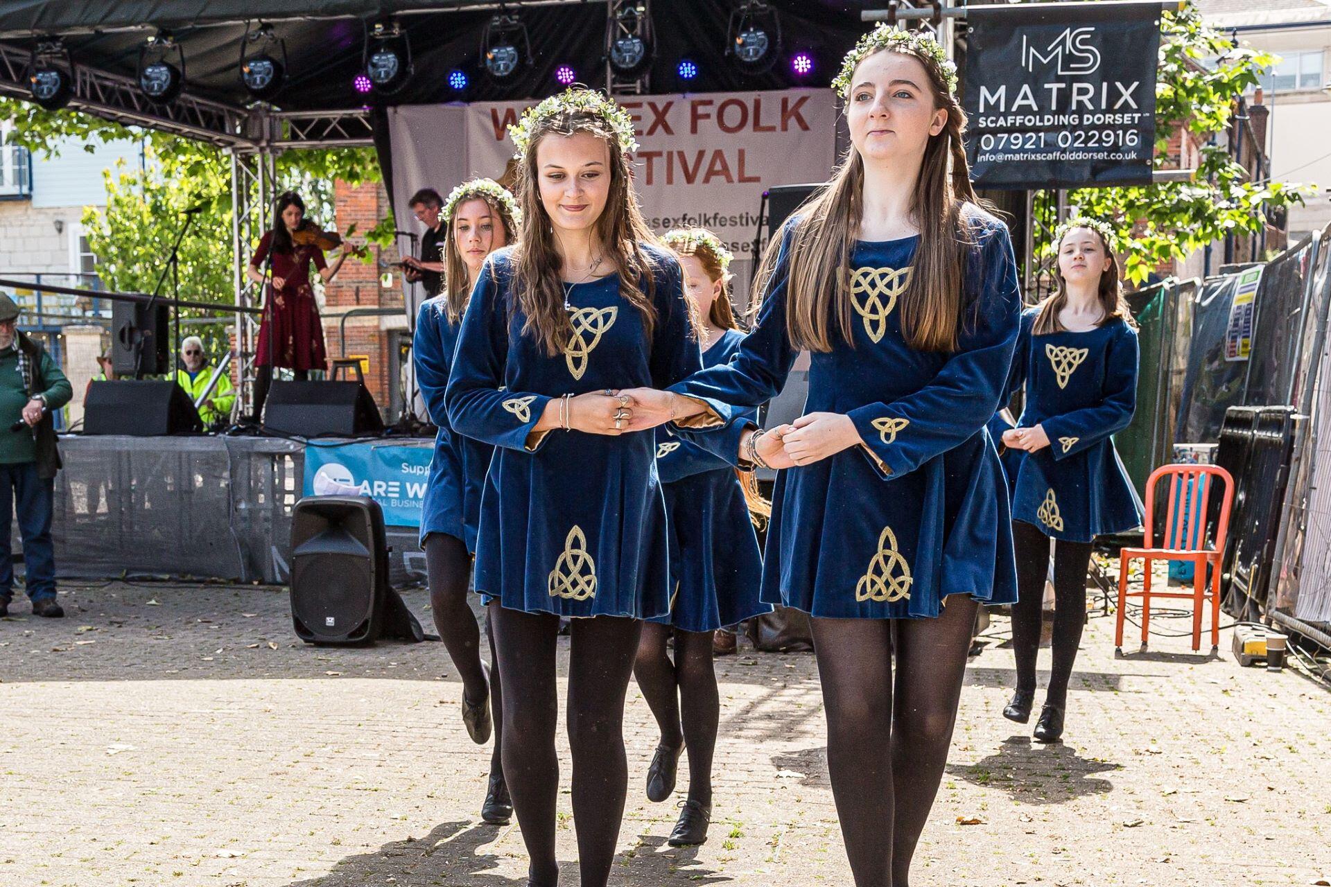 Group of young dancers in matching navy dresses performing at an outdoor festival