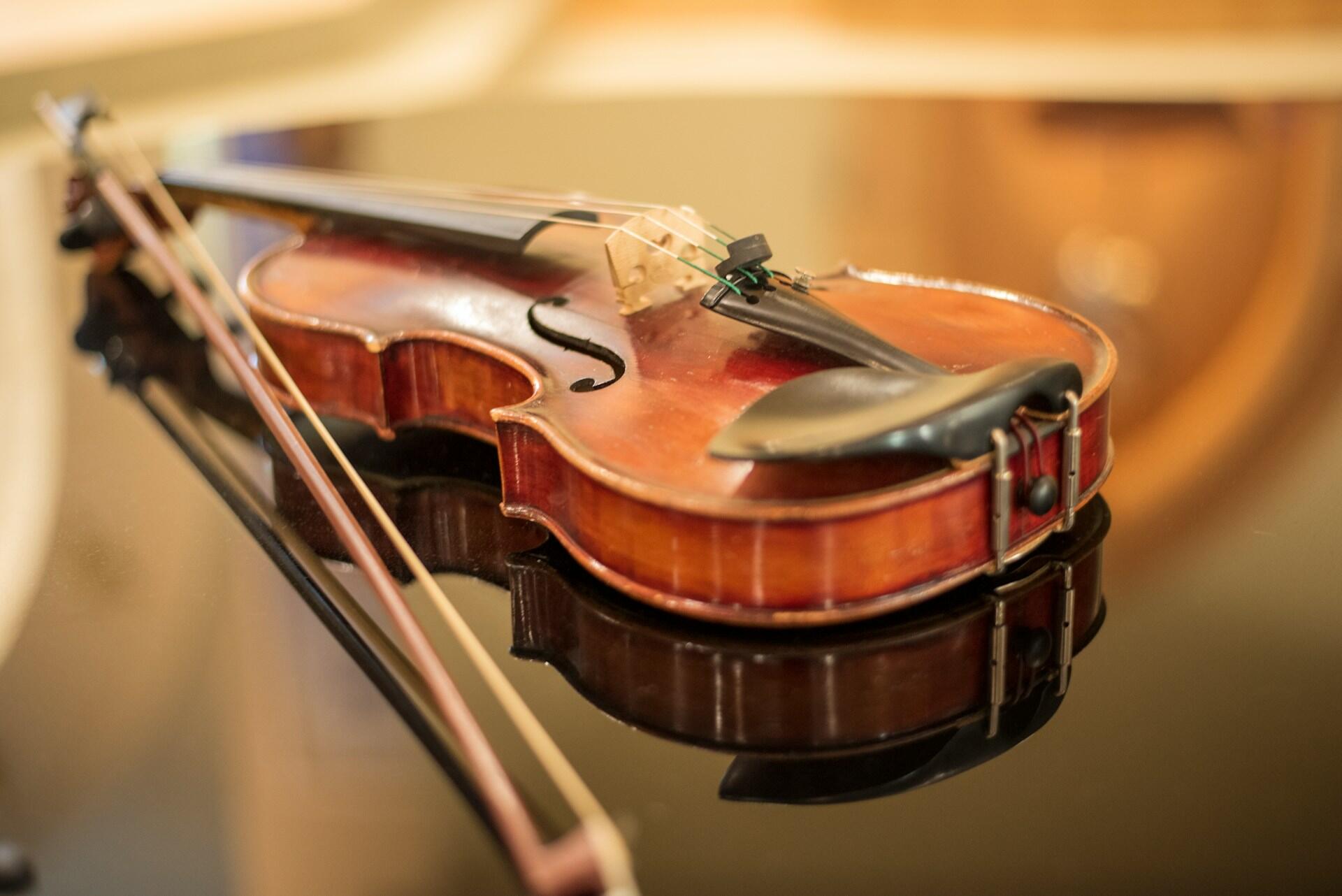 Wooden violin and bow resting on a reflective black surface