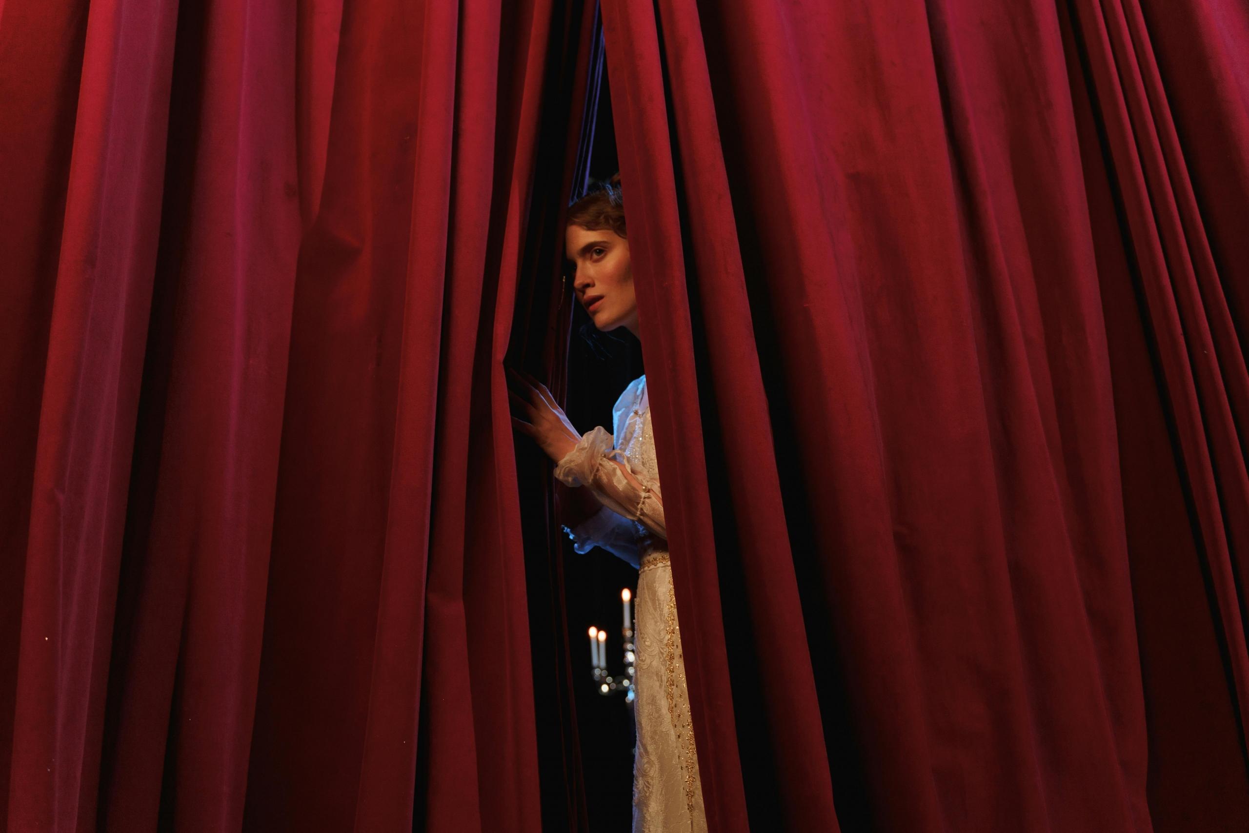 An actor pulls back the curtain to reveal a live audience awaiting her performance.