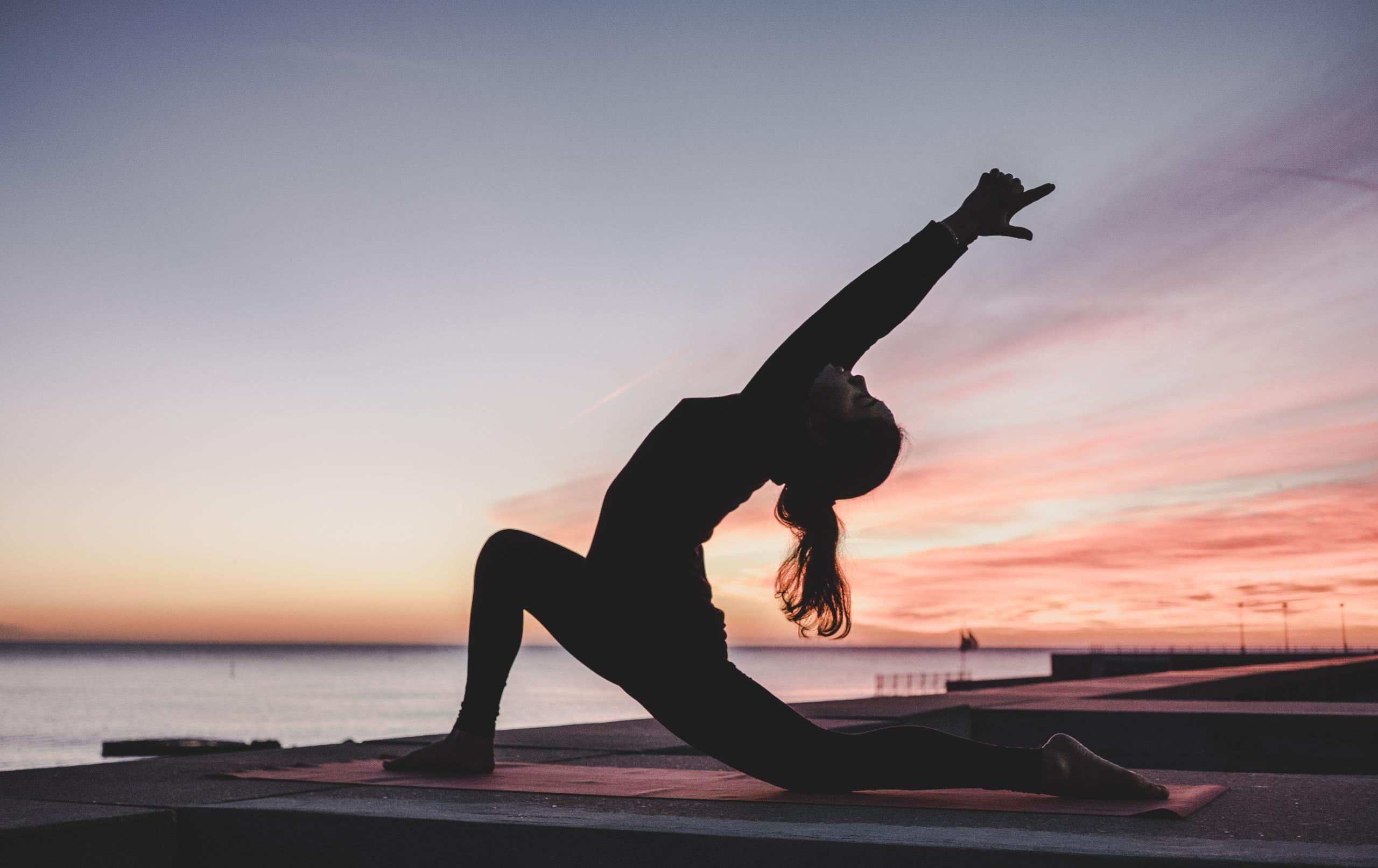 A woman practicing yoga next to the sea at sunset