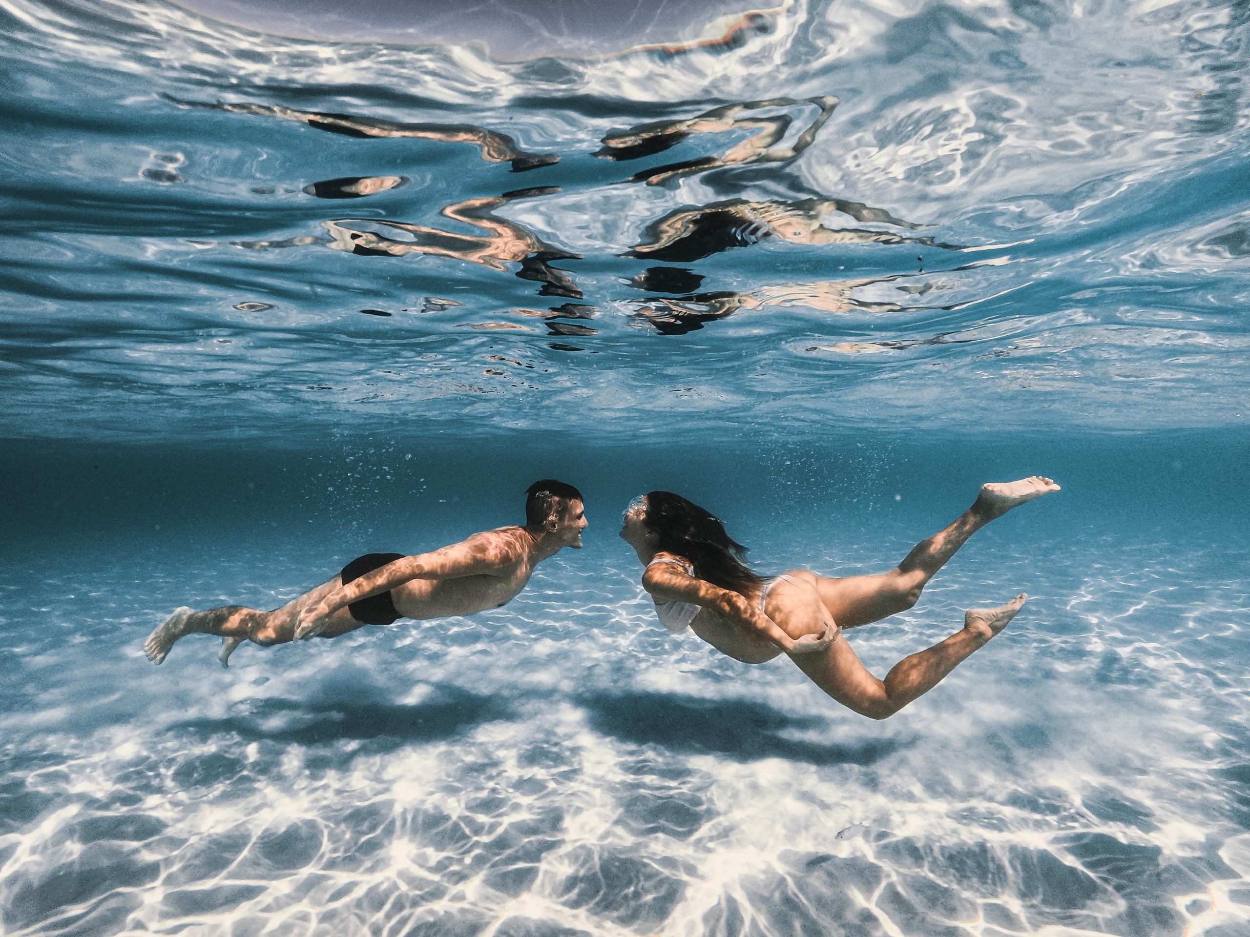 A beautifully captured moment of a pregnant woman gliding through the water with a serene expression, finding comfort and tranquility in prenatal swimming