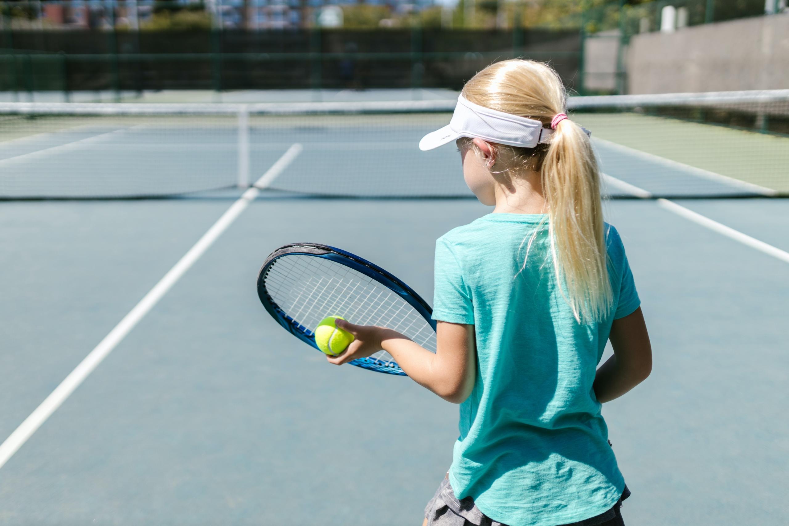 A young girl holding a tennis ball and tennis racket on her hand