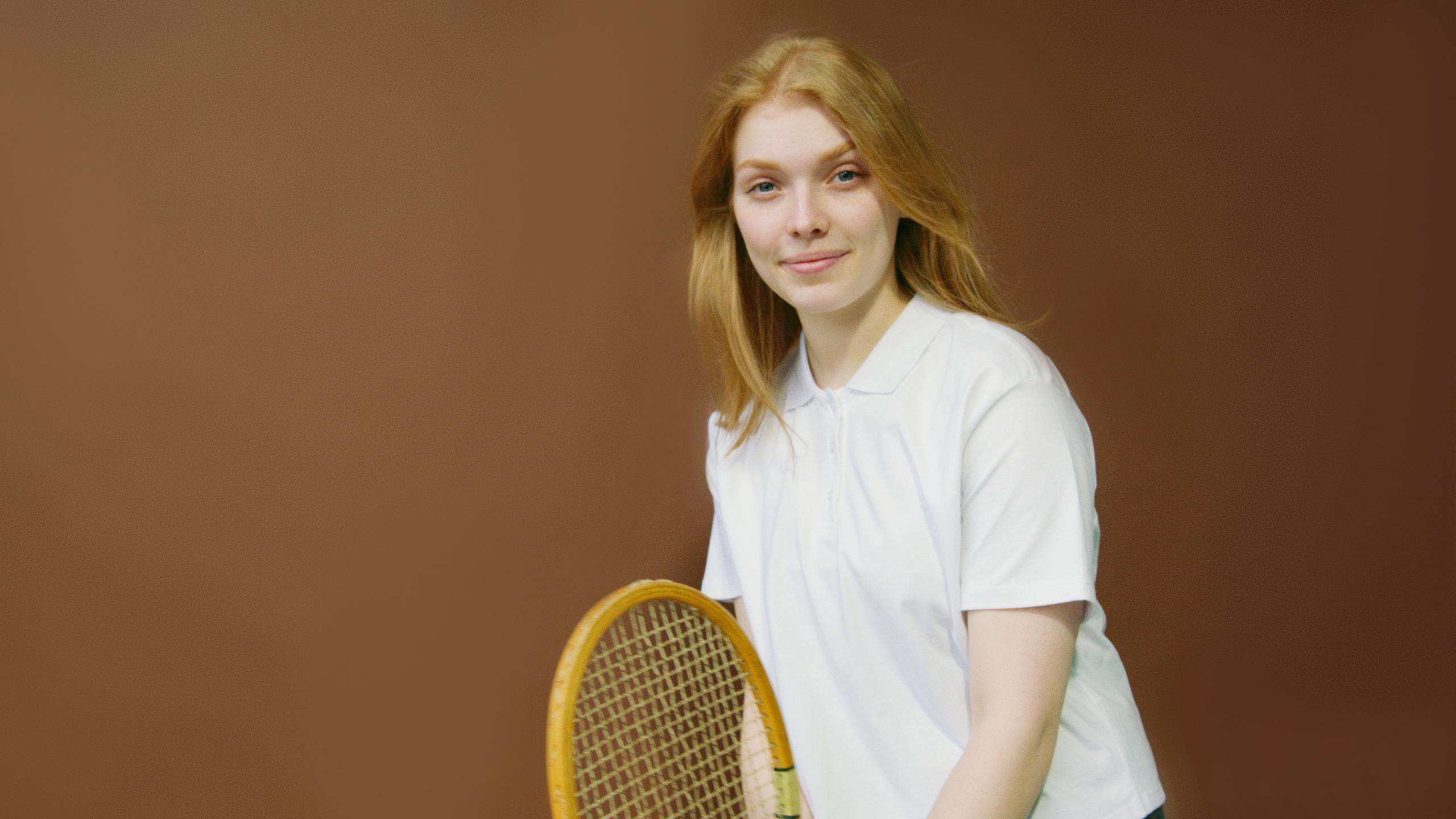 Player's hand gripping the handle of a tennis racket against a court backdrop.