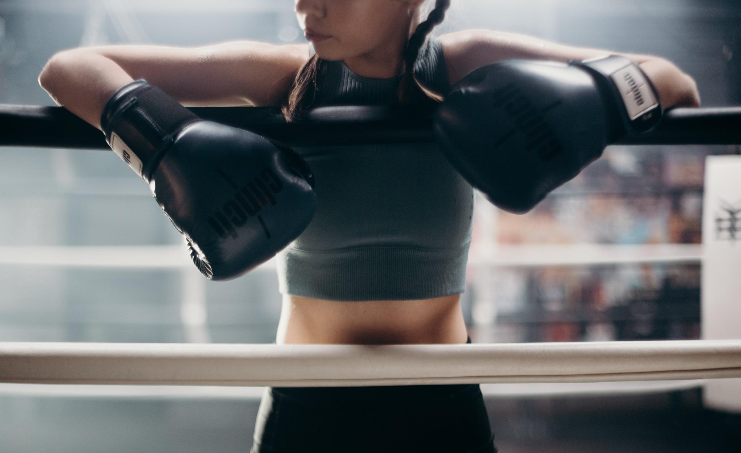 A boxer resting her arms on the ropes.