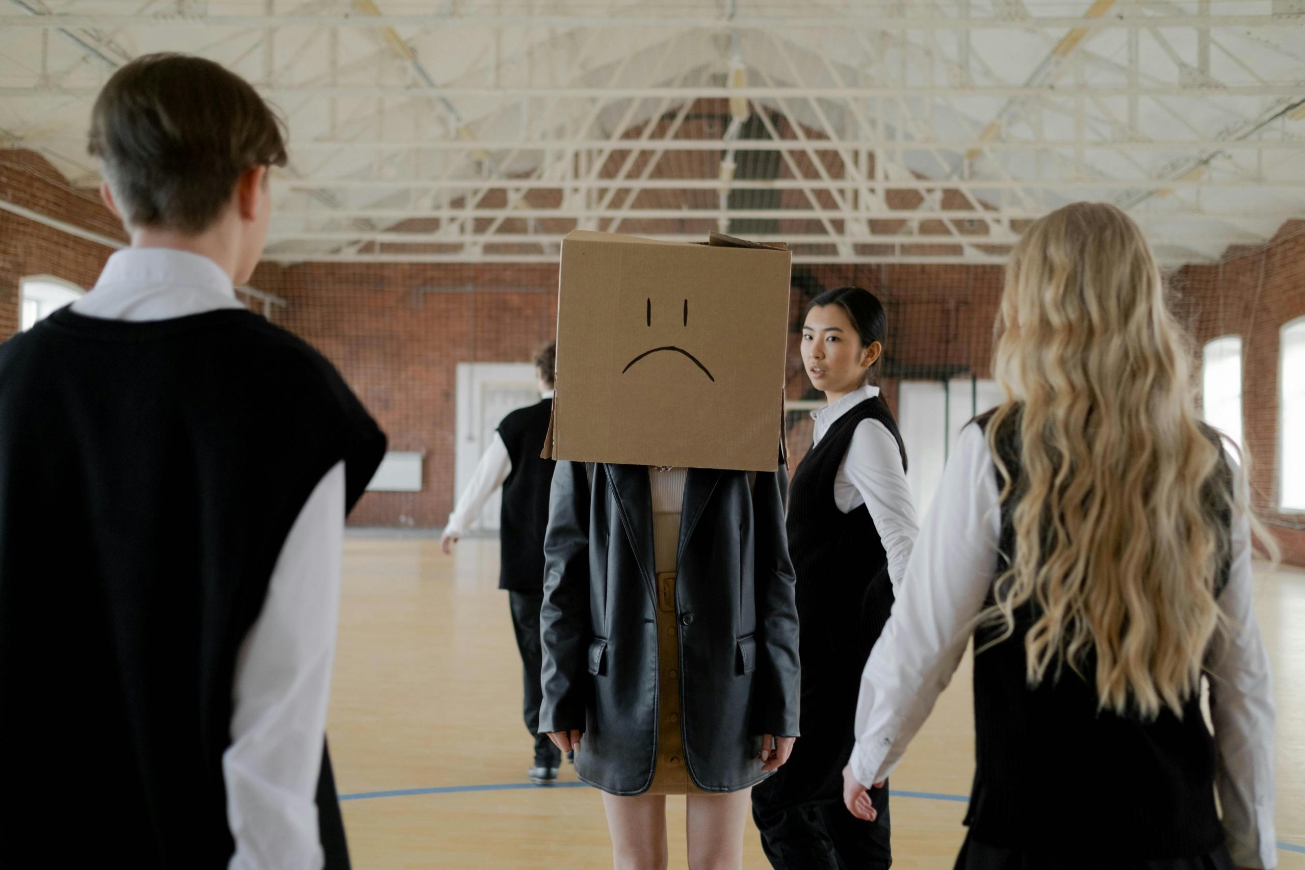 A student wearing a box with a frown face marked into the outside.