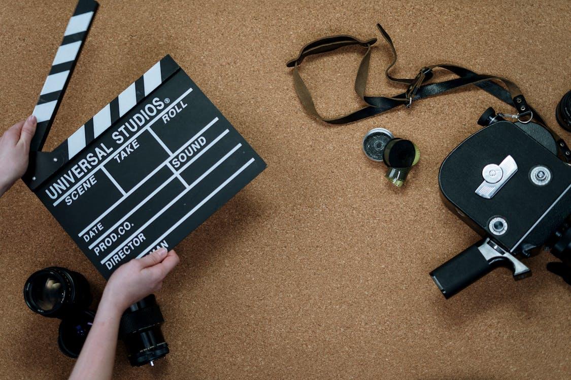 A hand holding a black clapperboard next to a vintage camera.