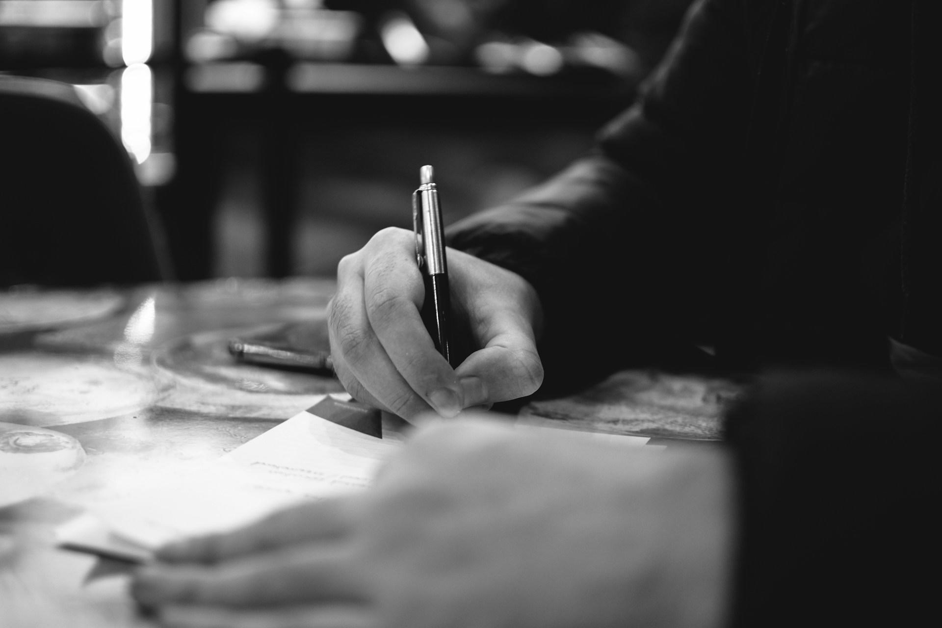 A closeup greyscale photo of somebody's hands while studying.