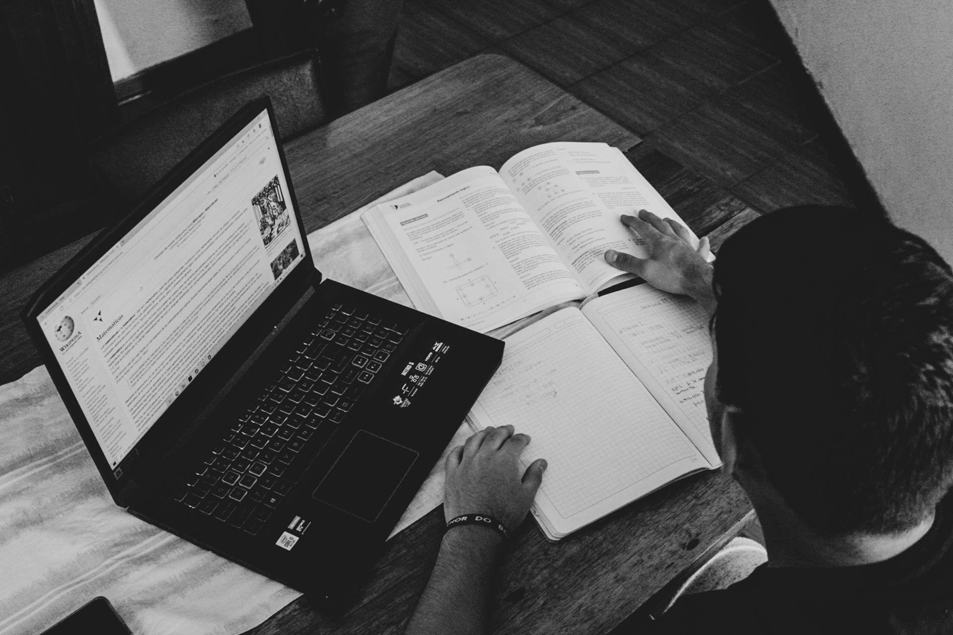 A greyscale photo of a man doing research from books and Wikipedia.