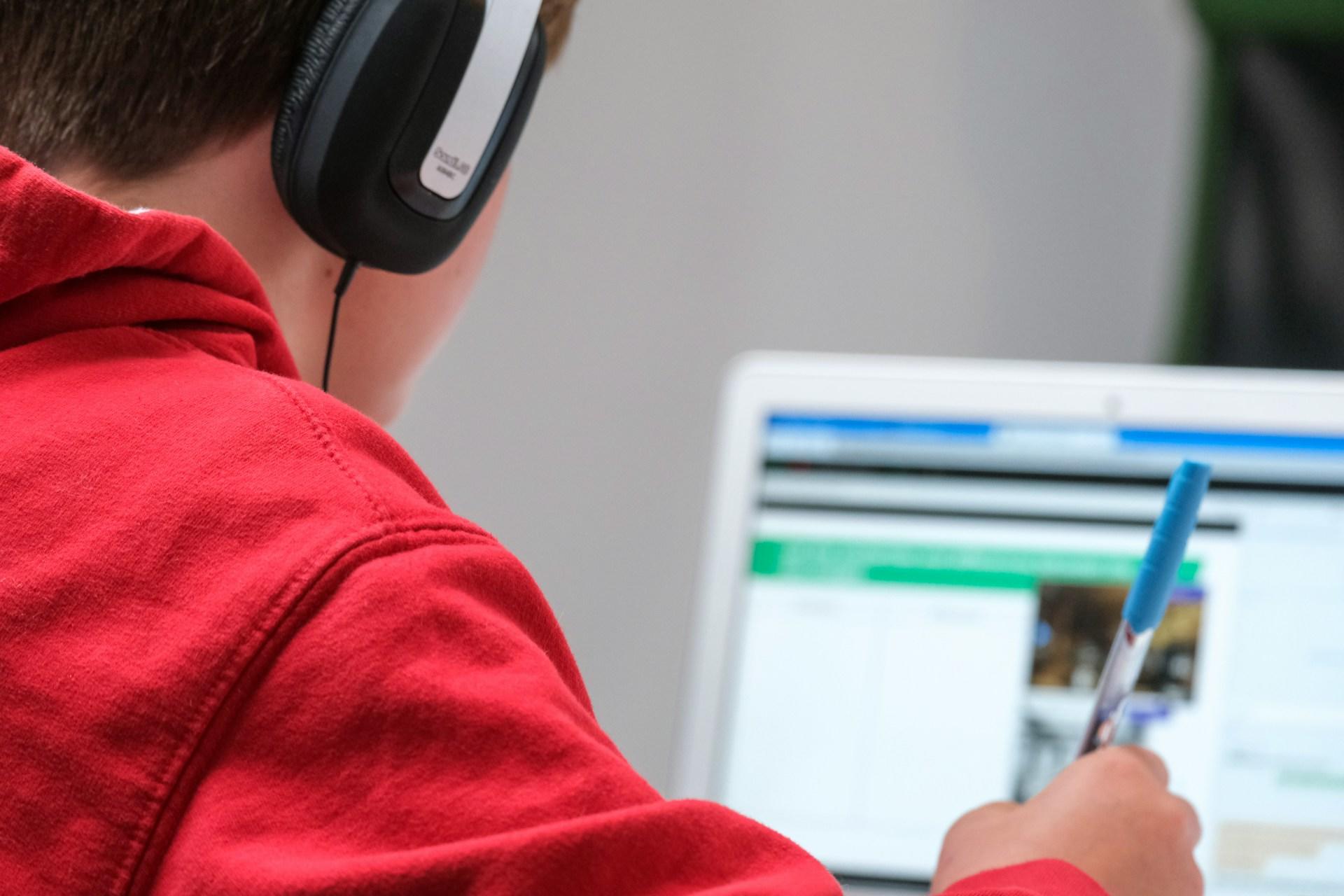 A boy in a red hoodie using a laptop.