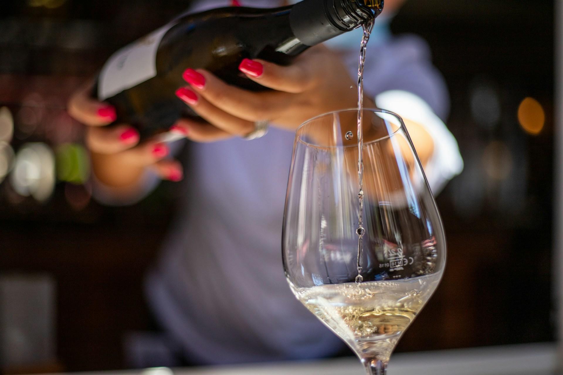 A waitress serving a glass of champagne or white wine.