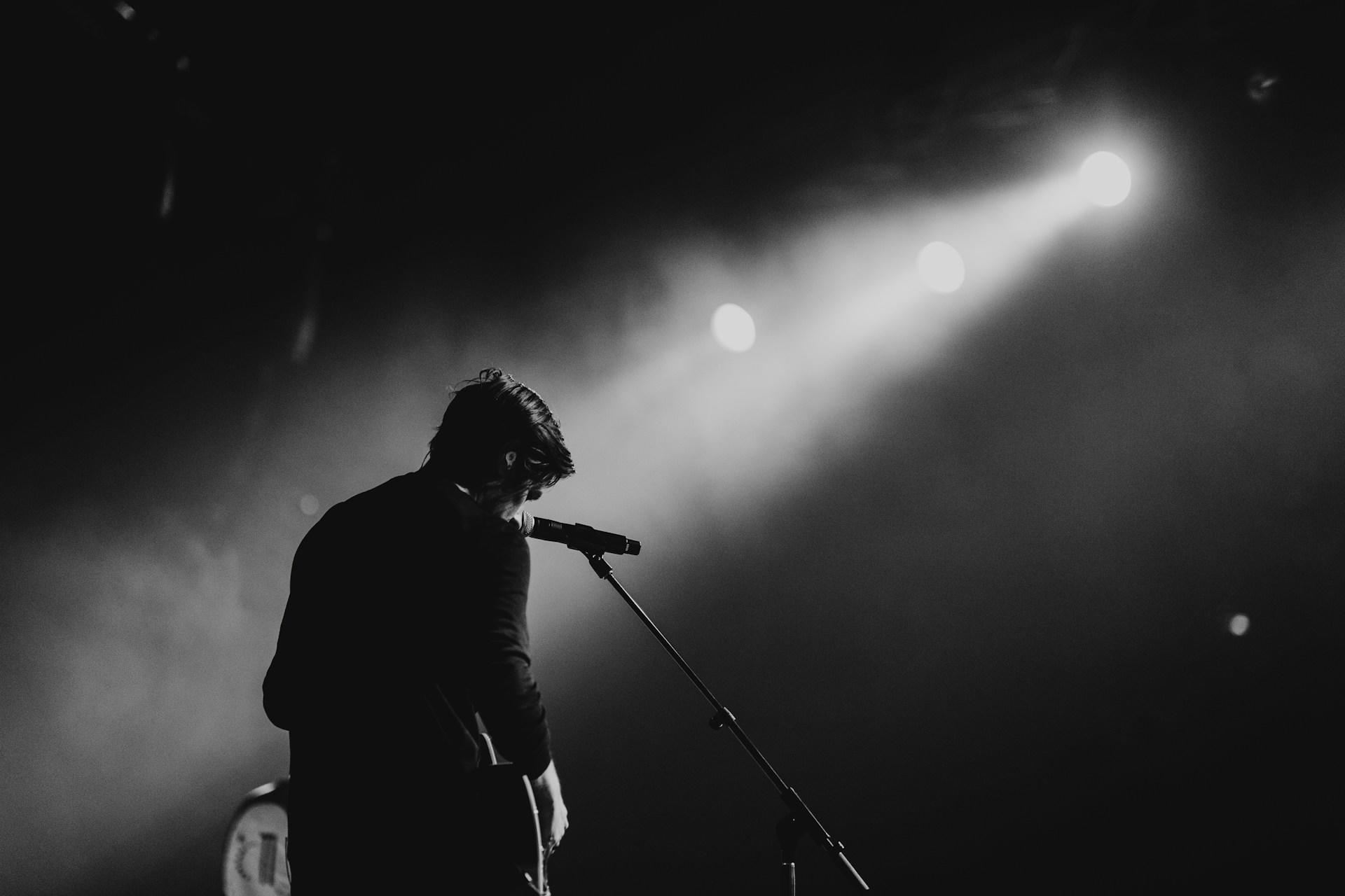 A man singing on stage through smoke.