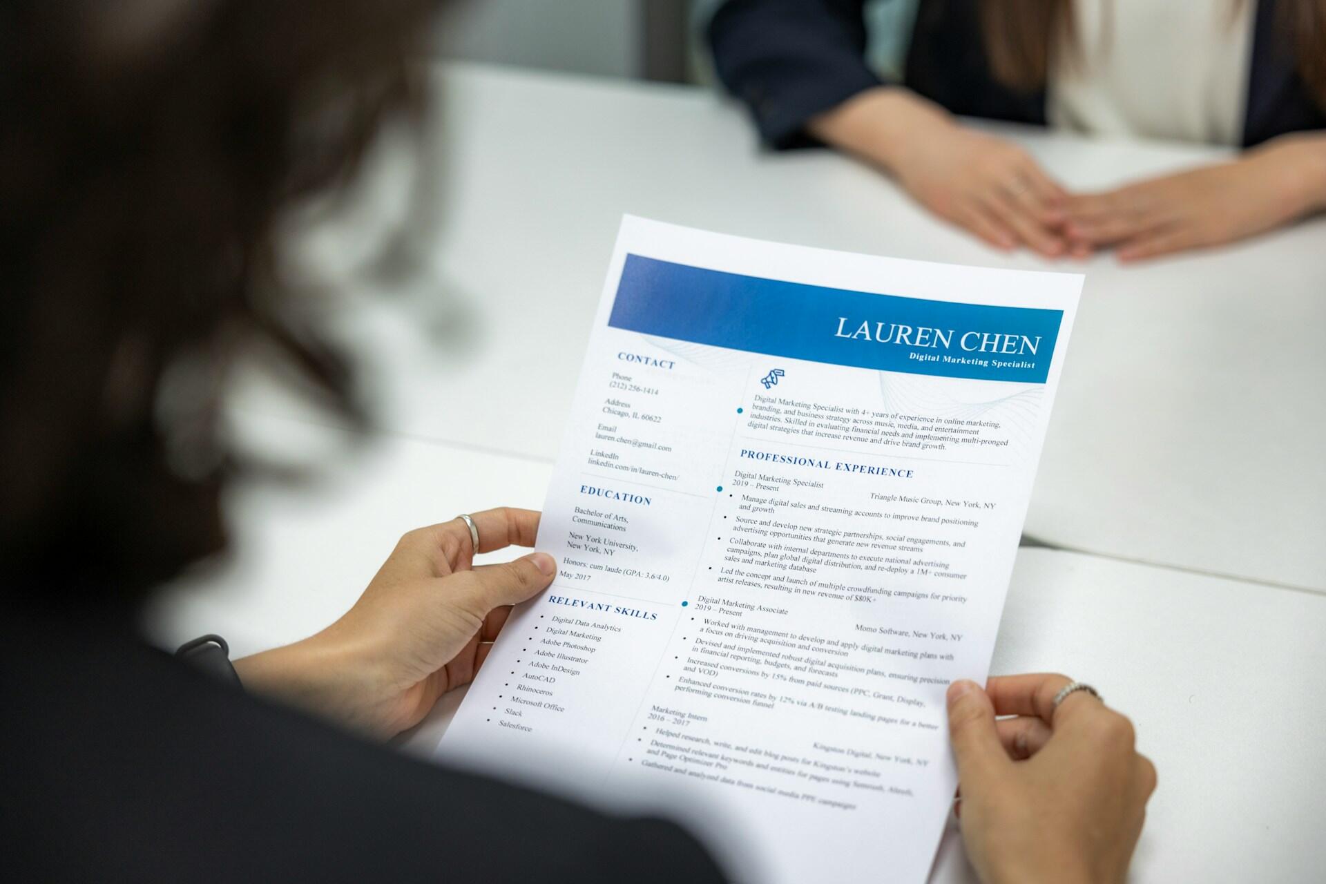 A person holding a printed CV across a table toward another person.