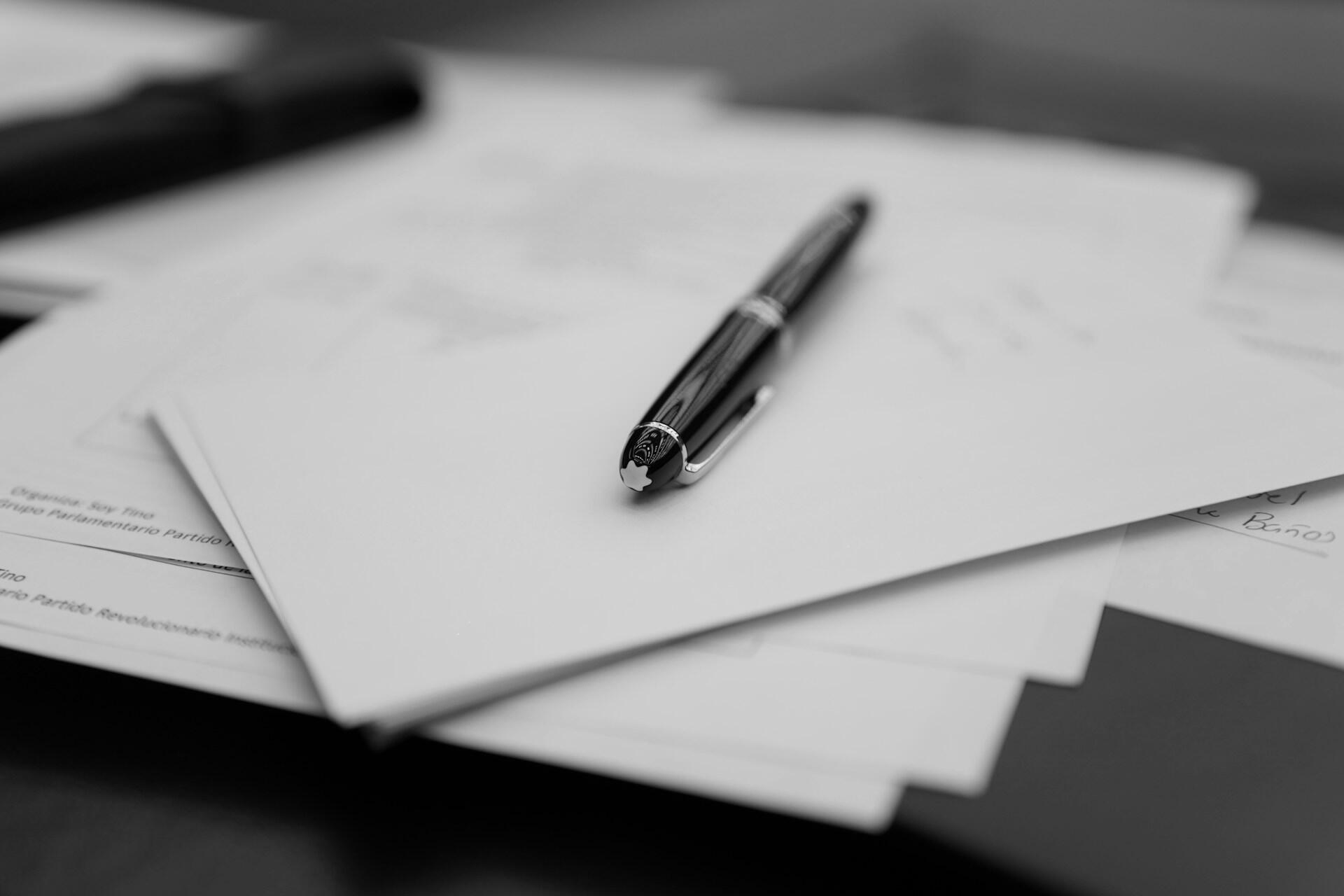 Black pen resting on top of printed papers on a desk