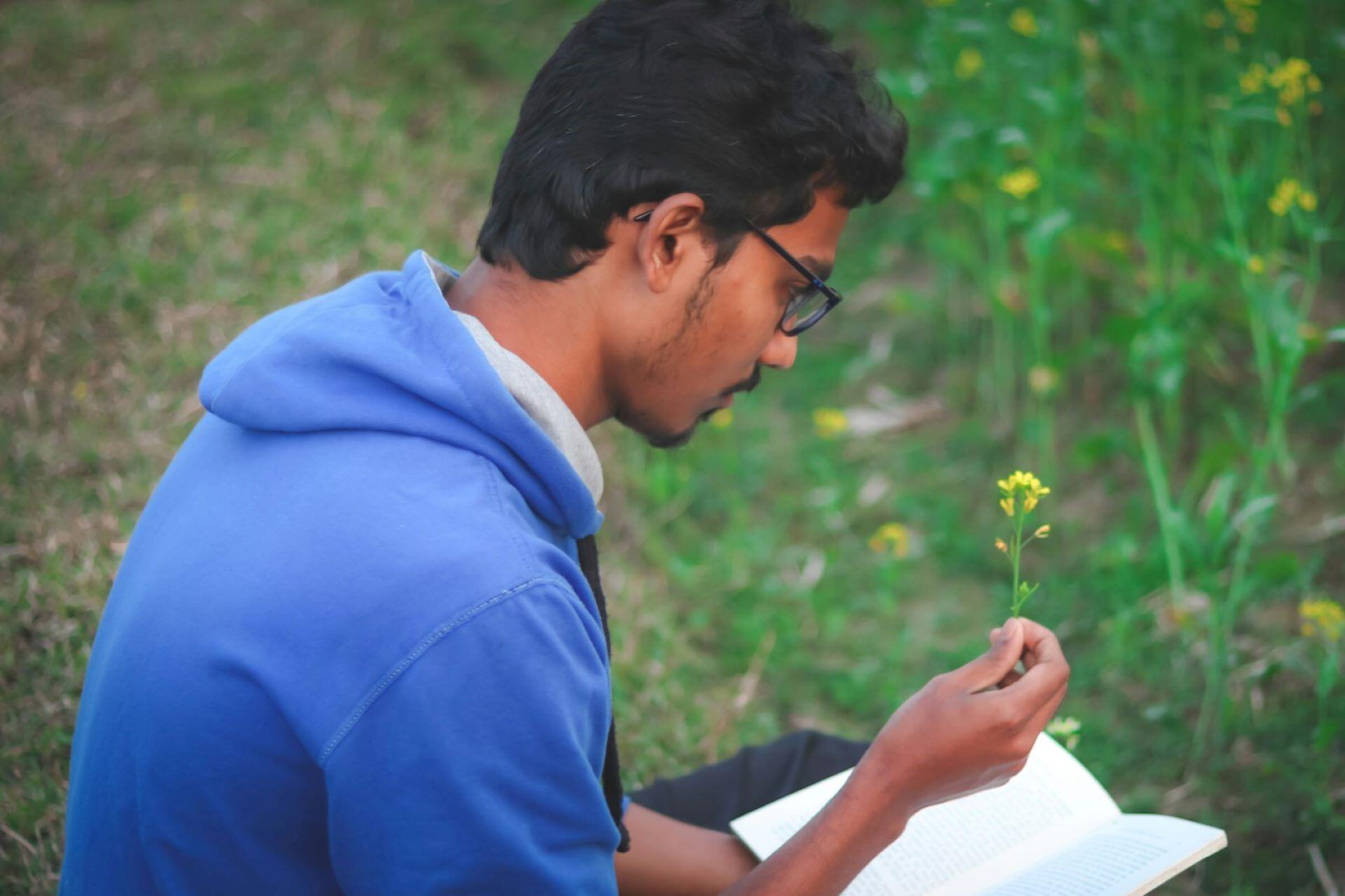 student reading book outdoors holding small yellow flower