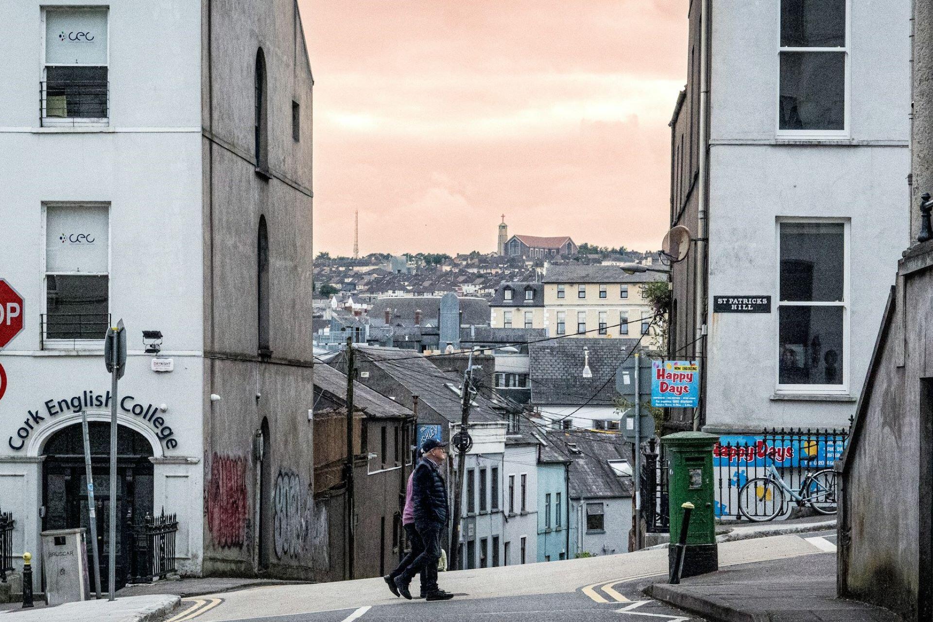 A person walking down a narrow street in Cork city with buildings and rooftops in the background