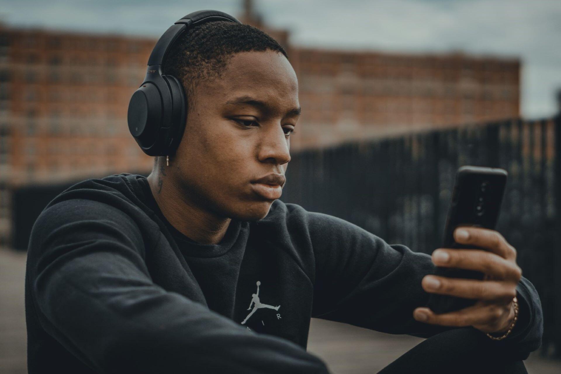 Person wearing black headphones and looking at a smartphone outdoors