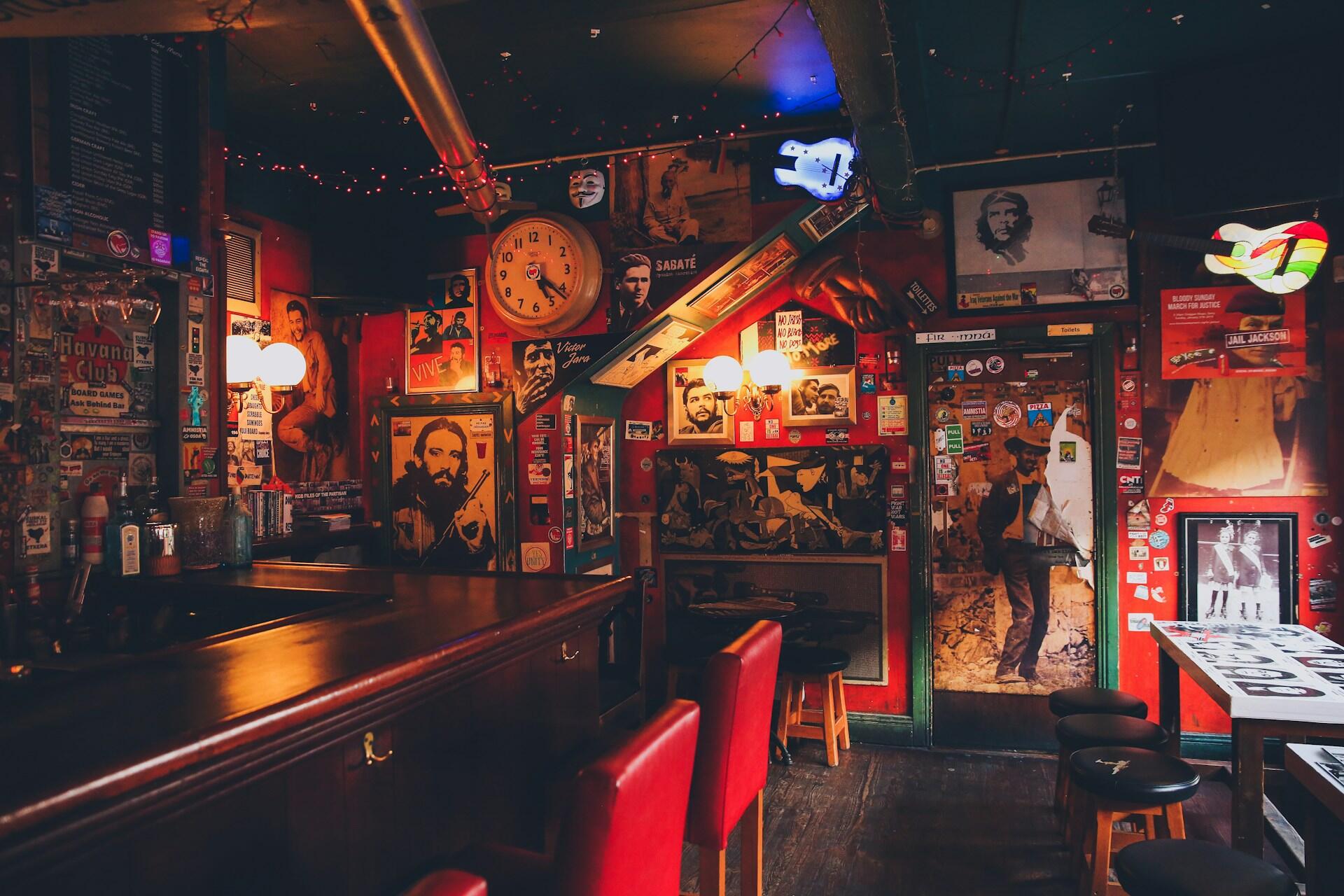 Interior of a pub with a bar counter, stools, and walls covered in posters and decorations