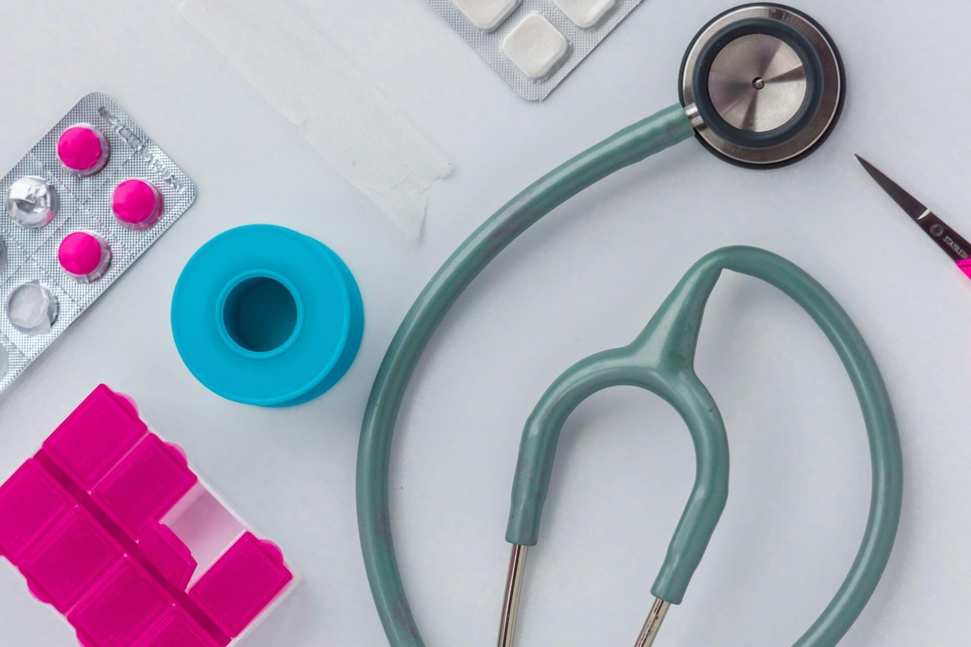 Stethoscope, medicine packets and medical supplies arranged on a white surface