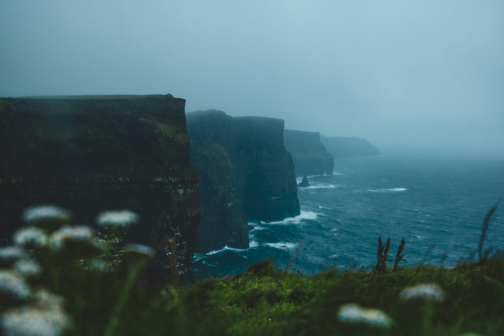 Rocky sea cliffs with ocean waves and mist under cloudy sky