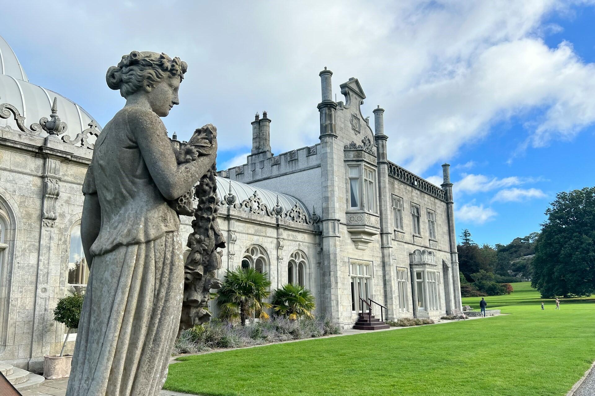 stone statue in front of a historic building with lawn and blue sky