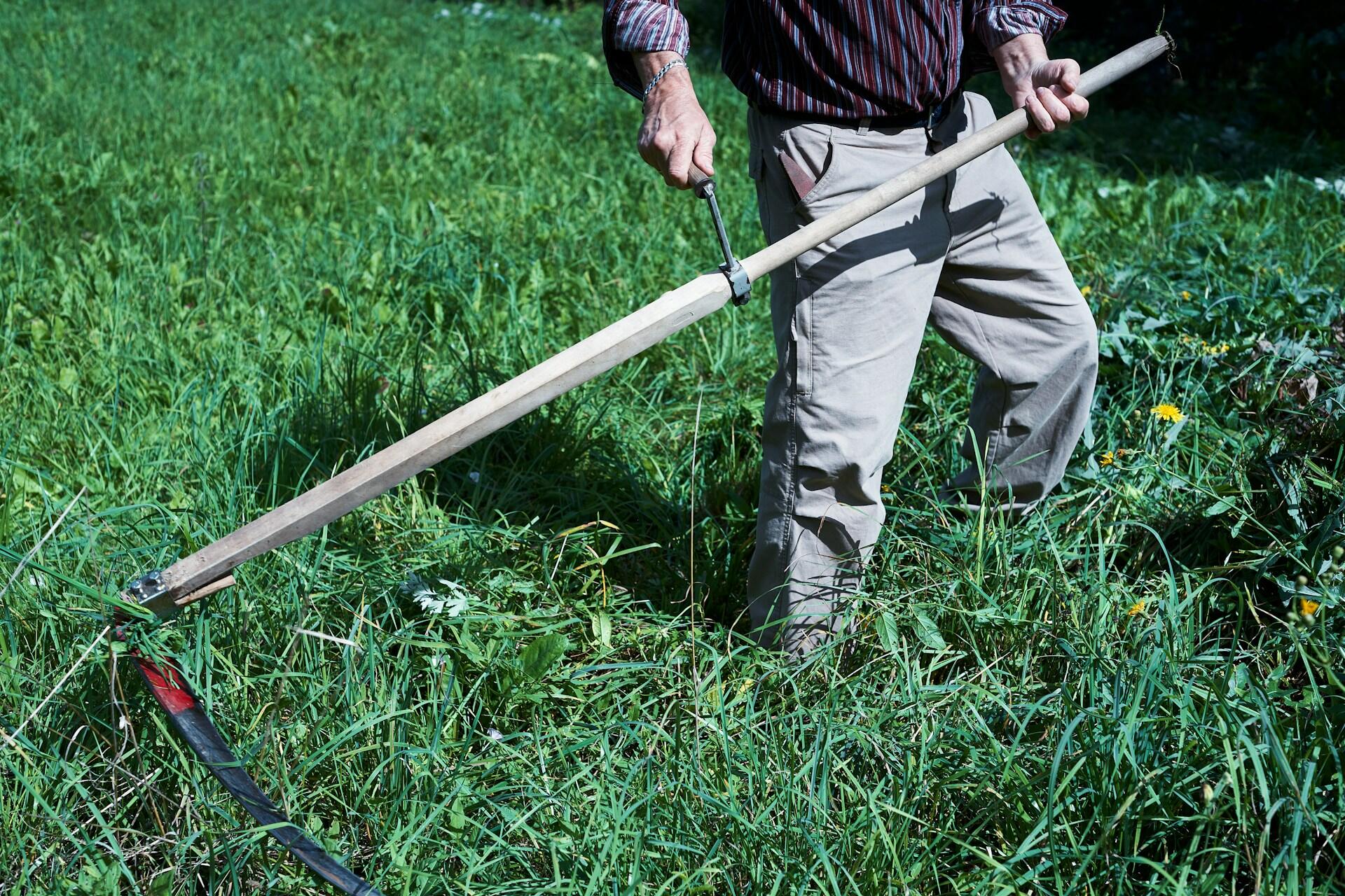 person using a scythe to cut grass in a field