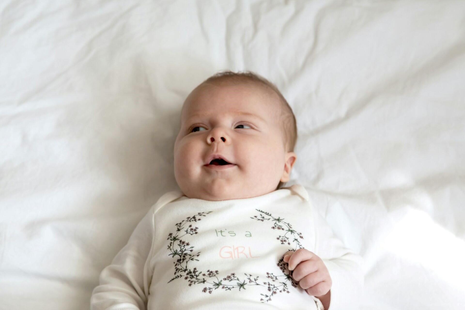 baby girl lying on white blanket wearing onesie
