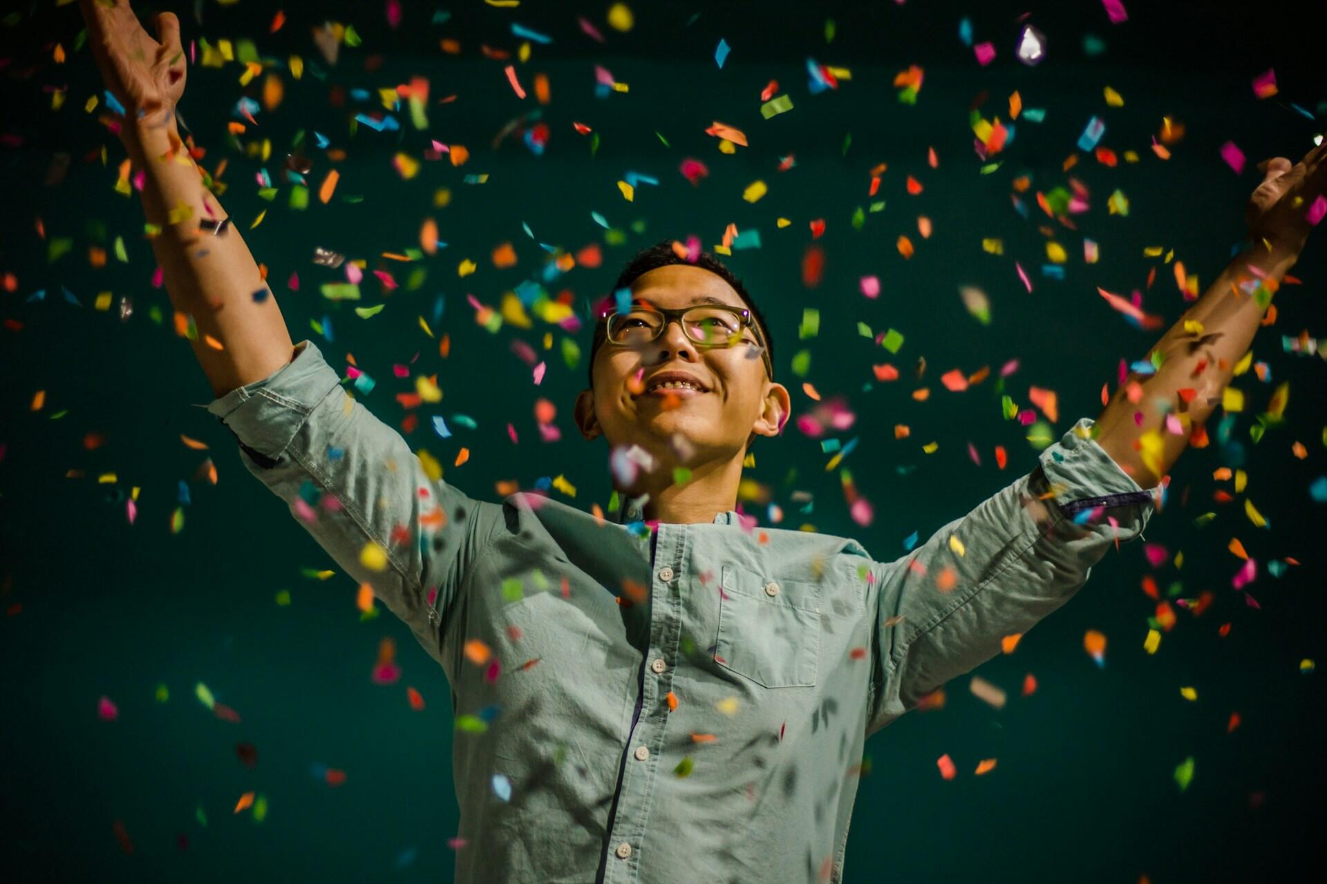 person celebrating with arms raised and confetti falling