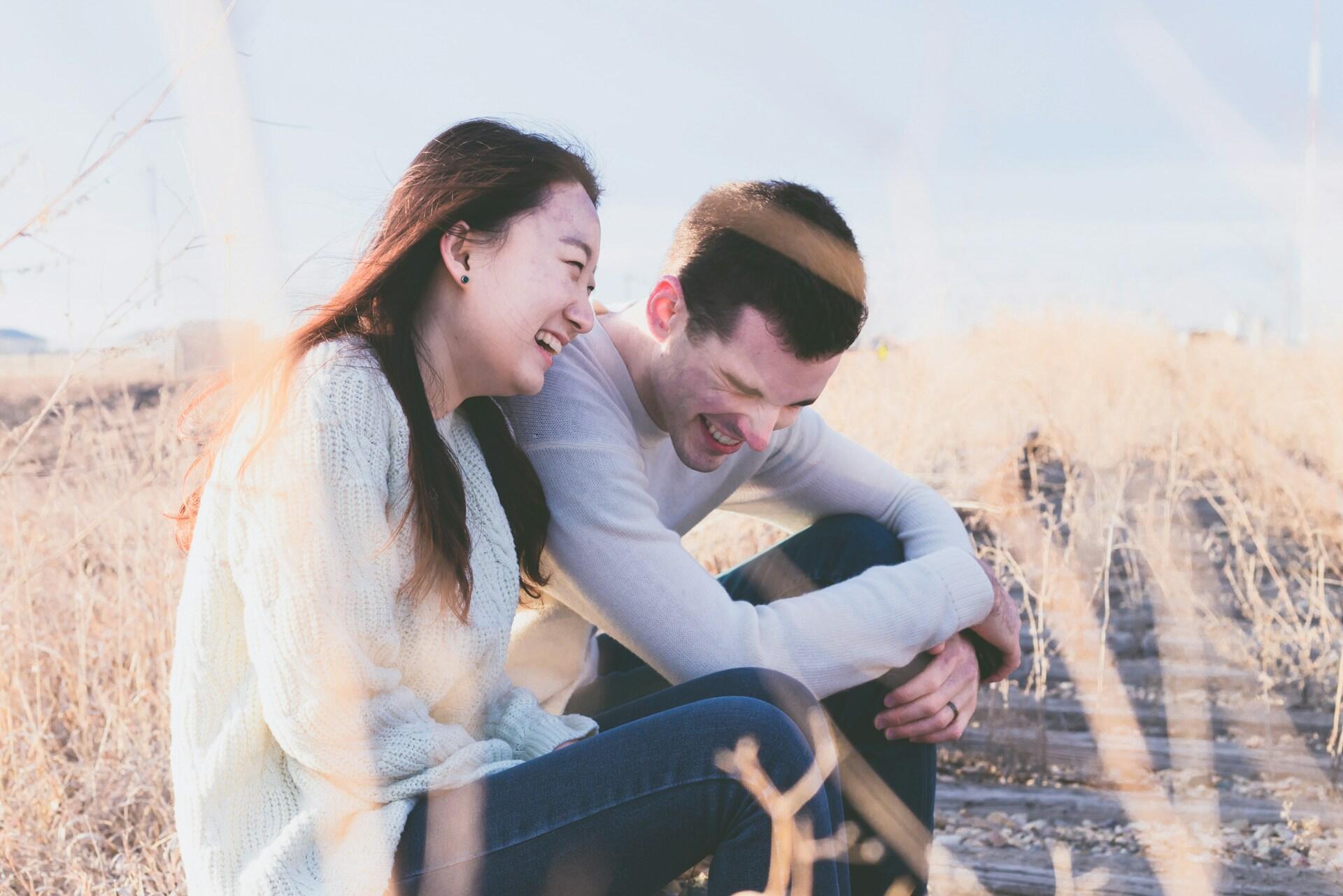 Couple sitting outdoors laughing together in a field