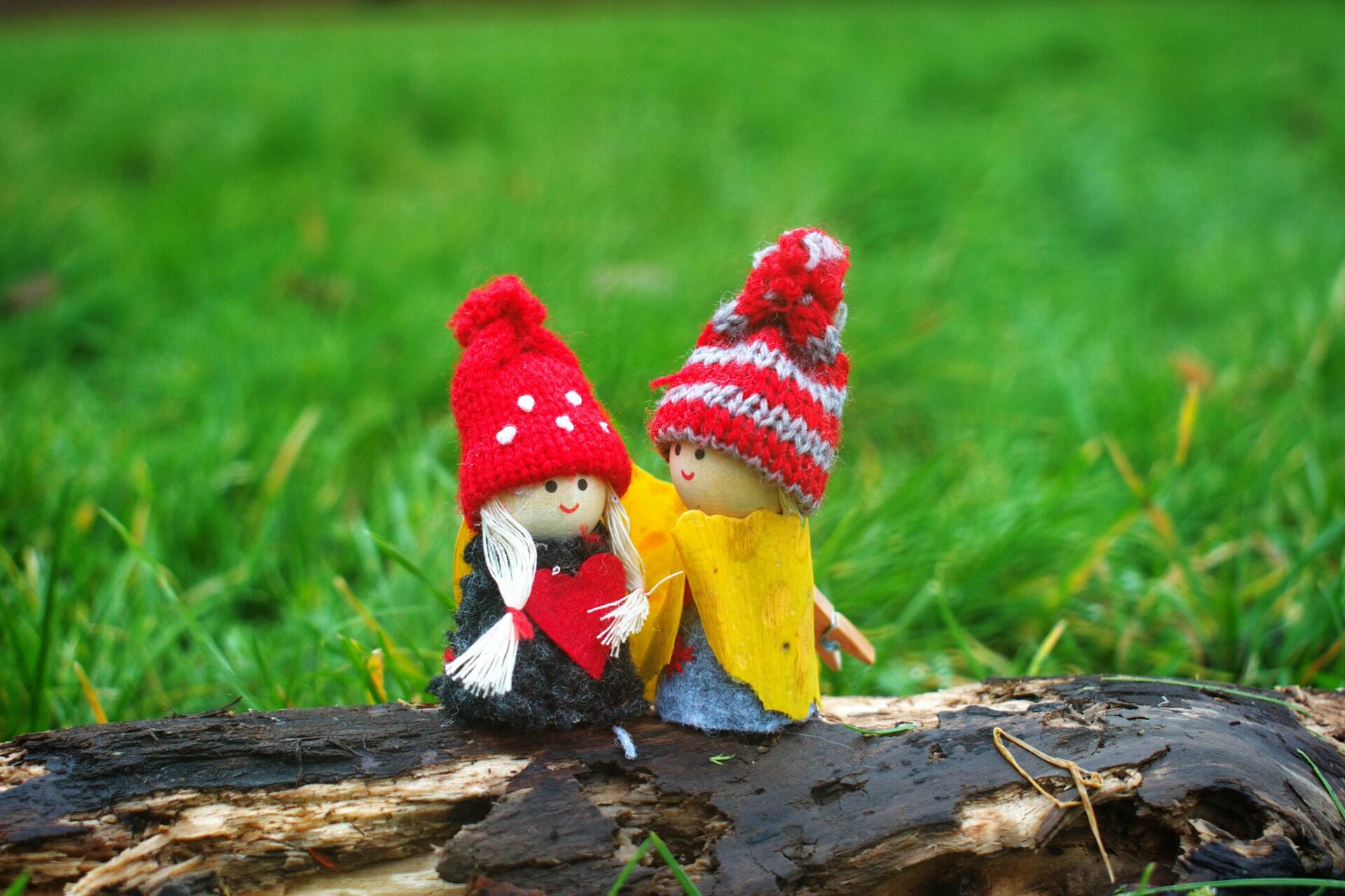 Two small dolls sitting together on a log wearing knitted hats.