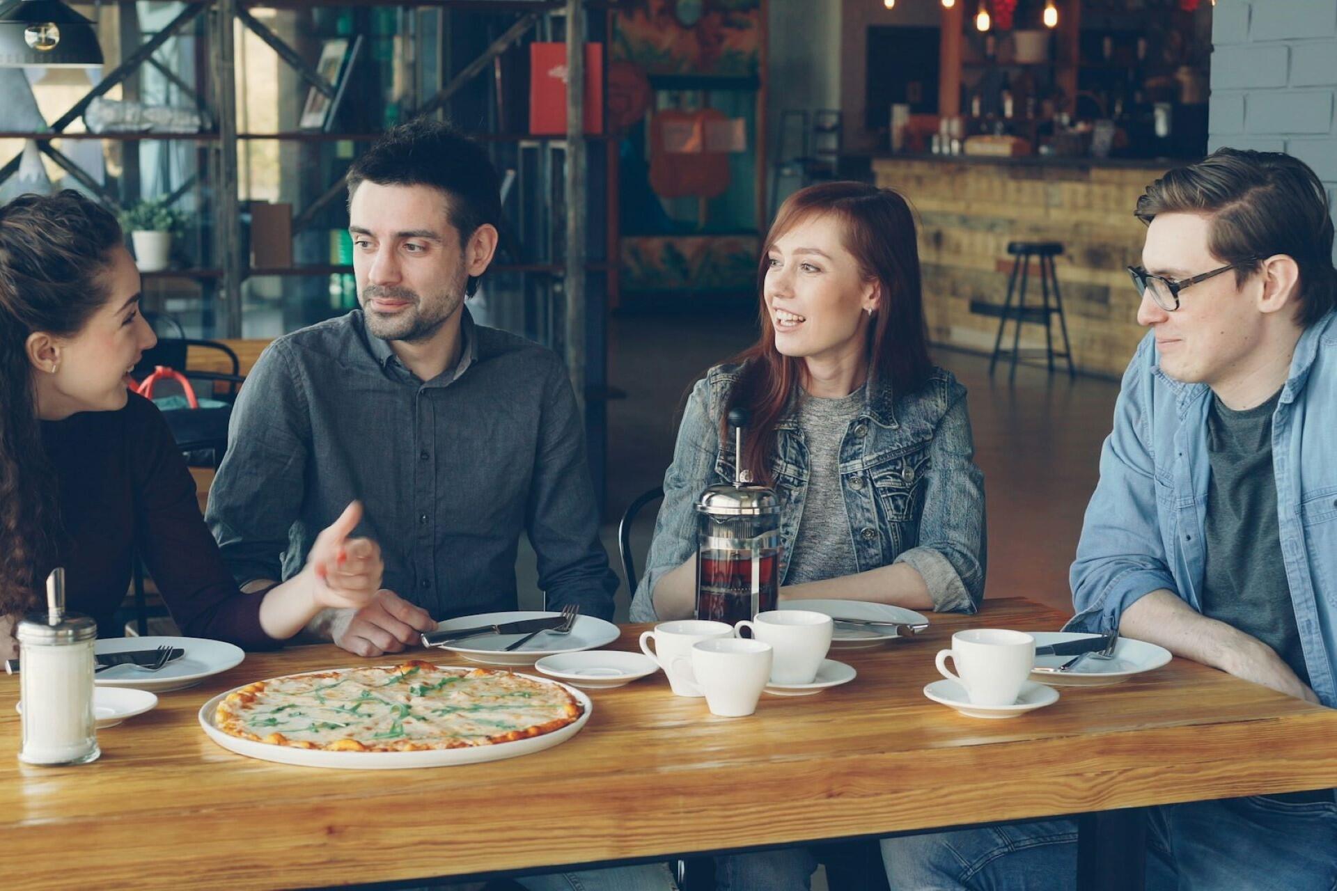 group of people sitting at a table talking and eating together