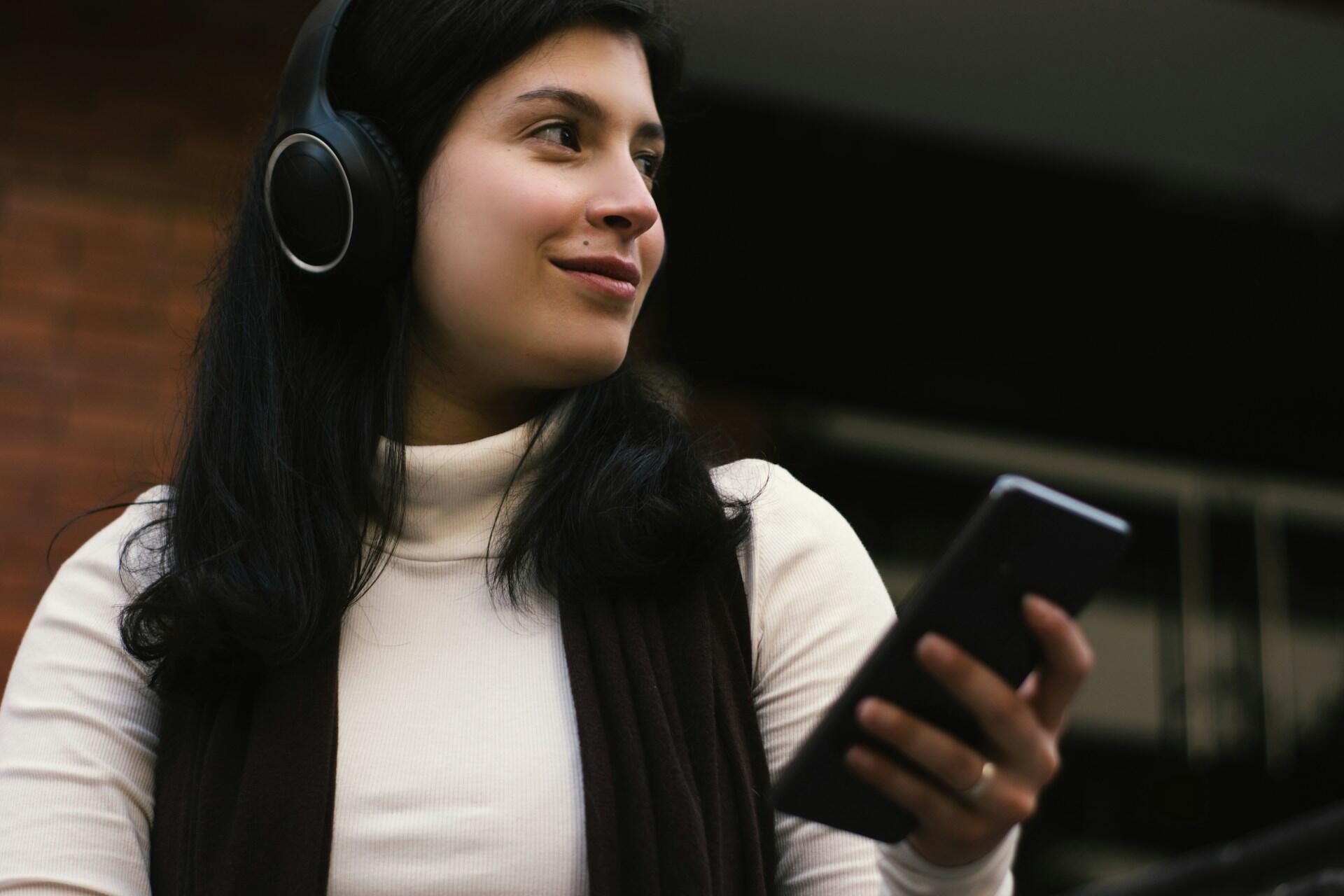 woman wearing headphones holding phone and listening
