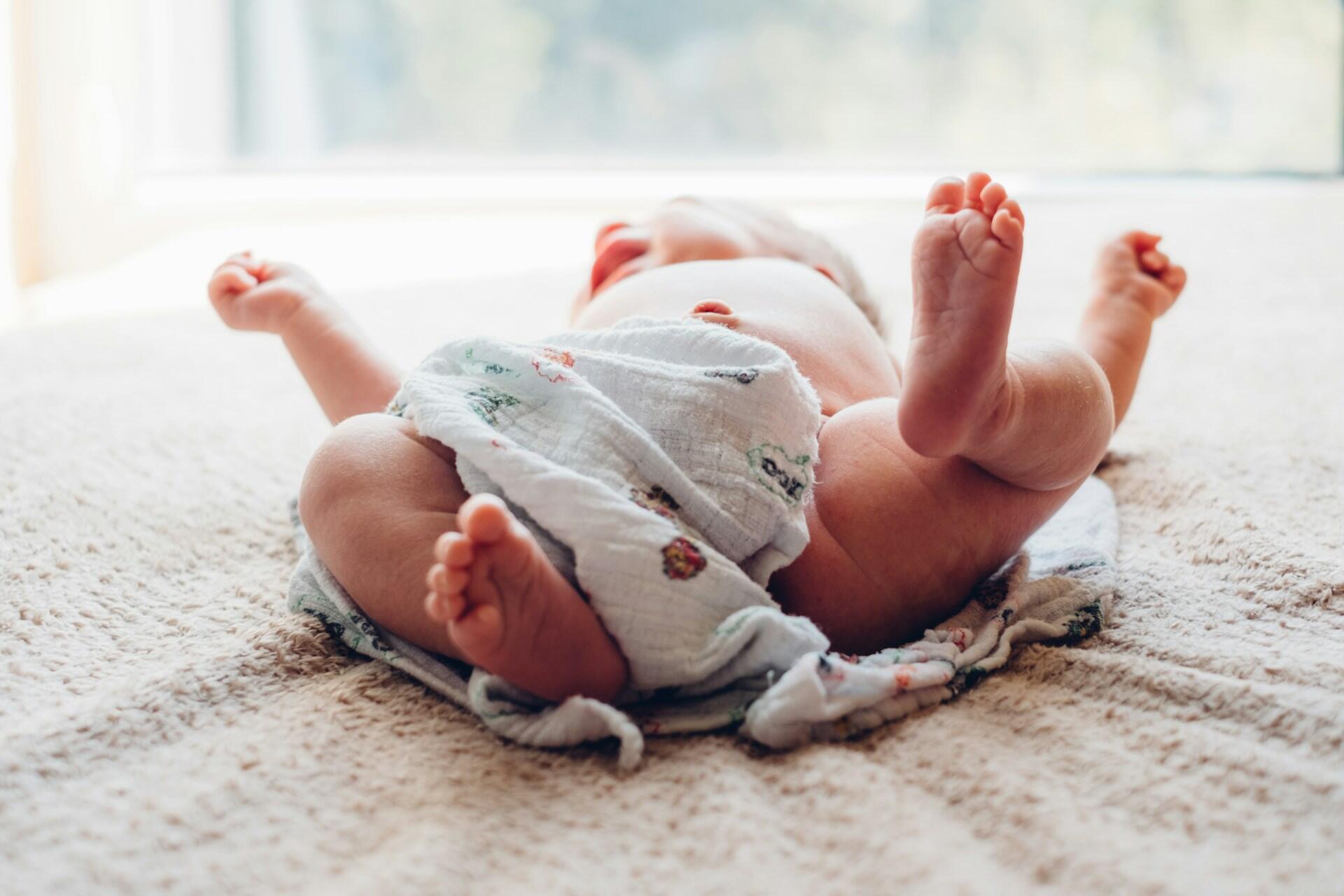 Newborn baby lying on a blanket with feet raised