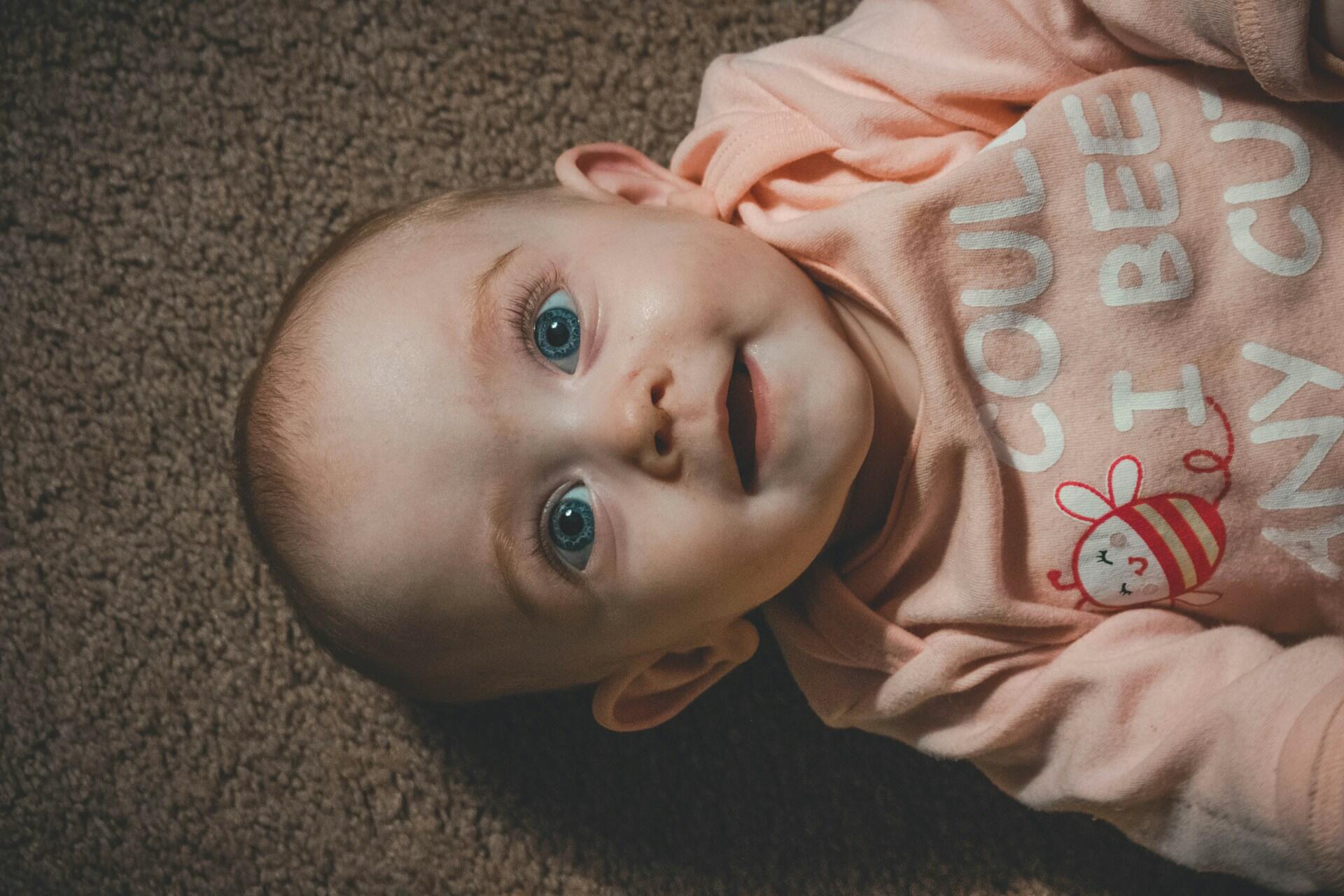 smiling baby girl lying on floor wearing pink outfit