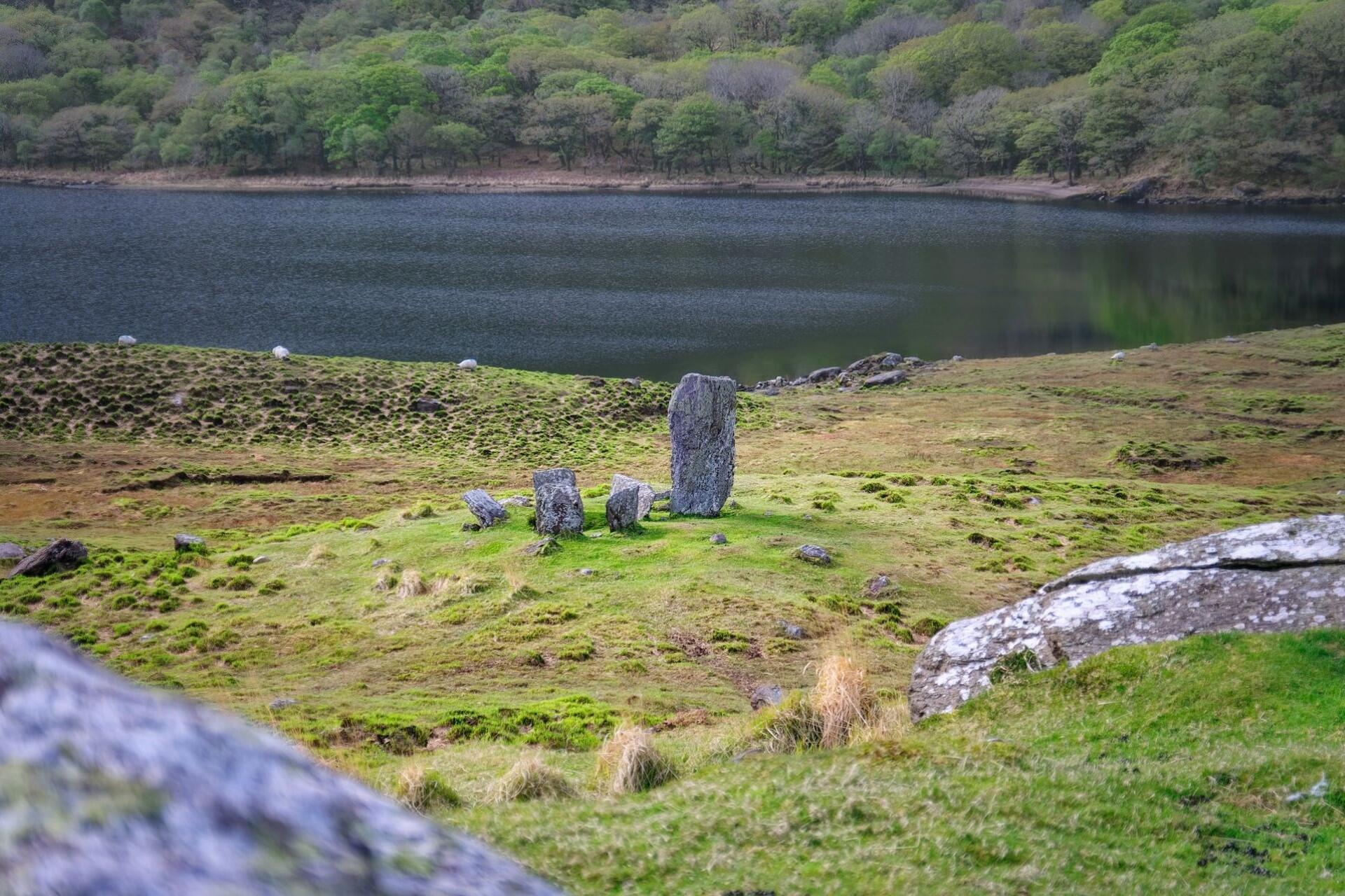 Stone circle beside a lake surrounded by green hills