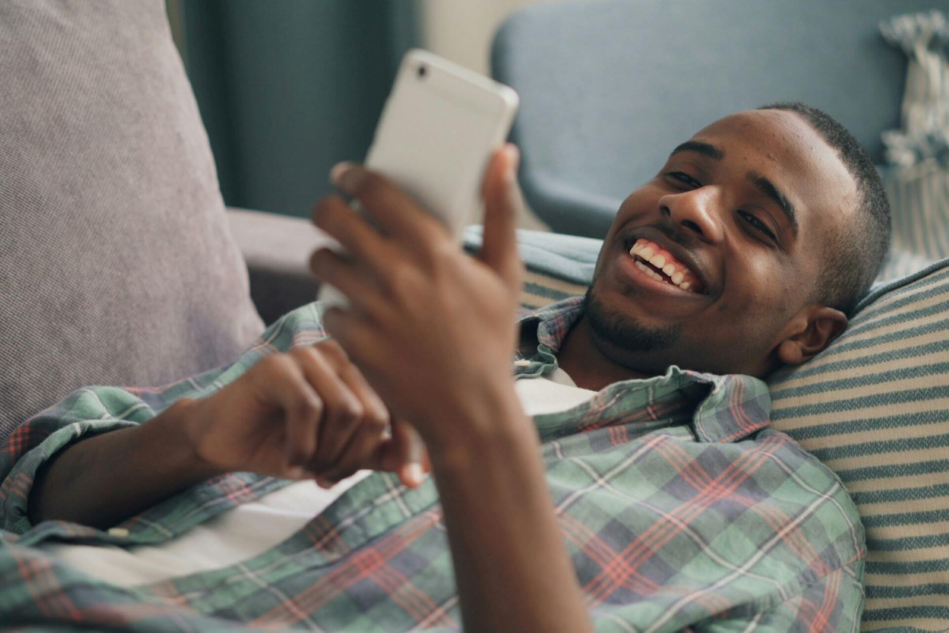 man smiling while looking at phone on sofa