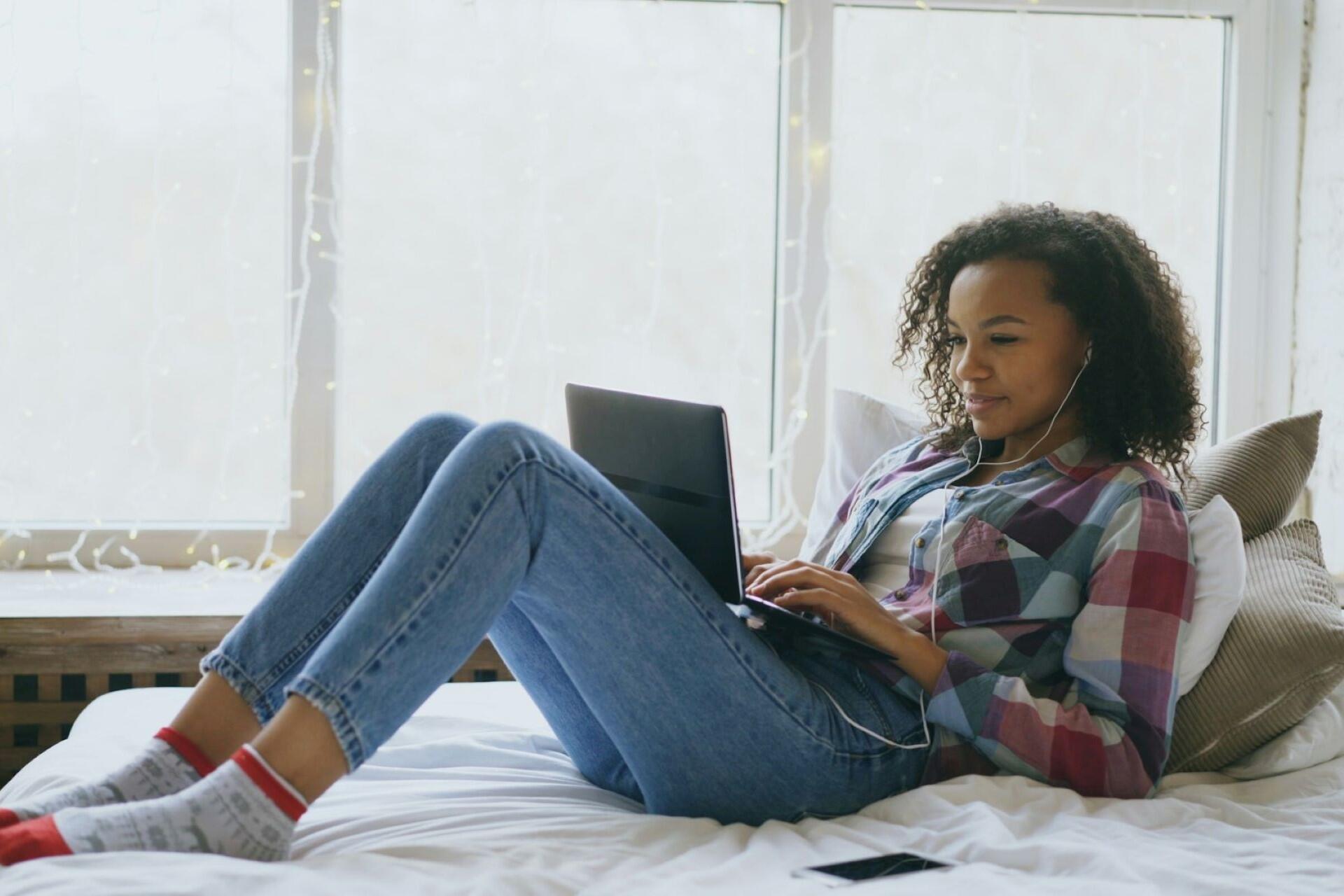 Young woman using a laptop and headphones on a bed